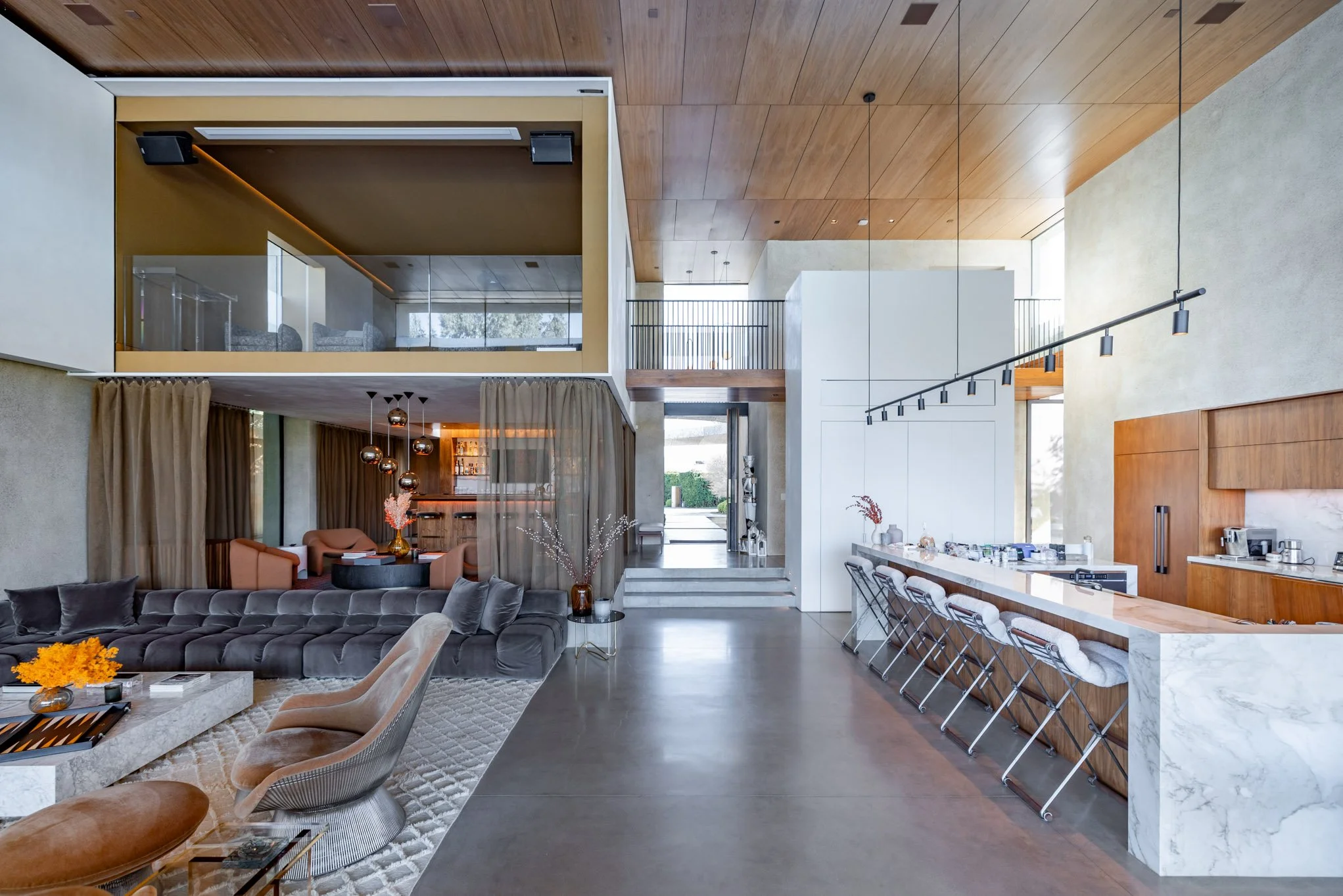 Modern open-concept living room and kitchen area in a house with high ceilings, wood accents, and contemporary furniture.