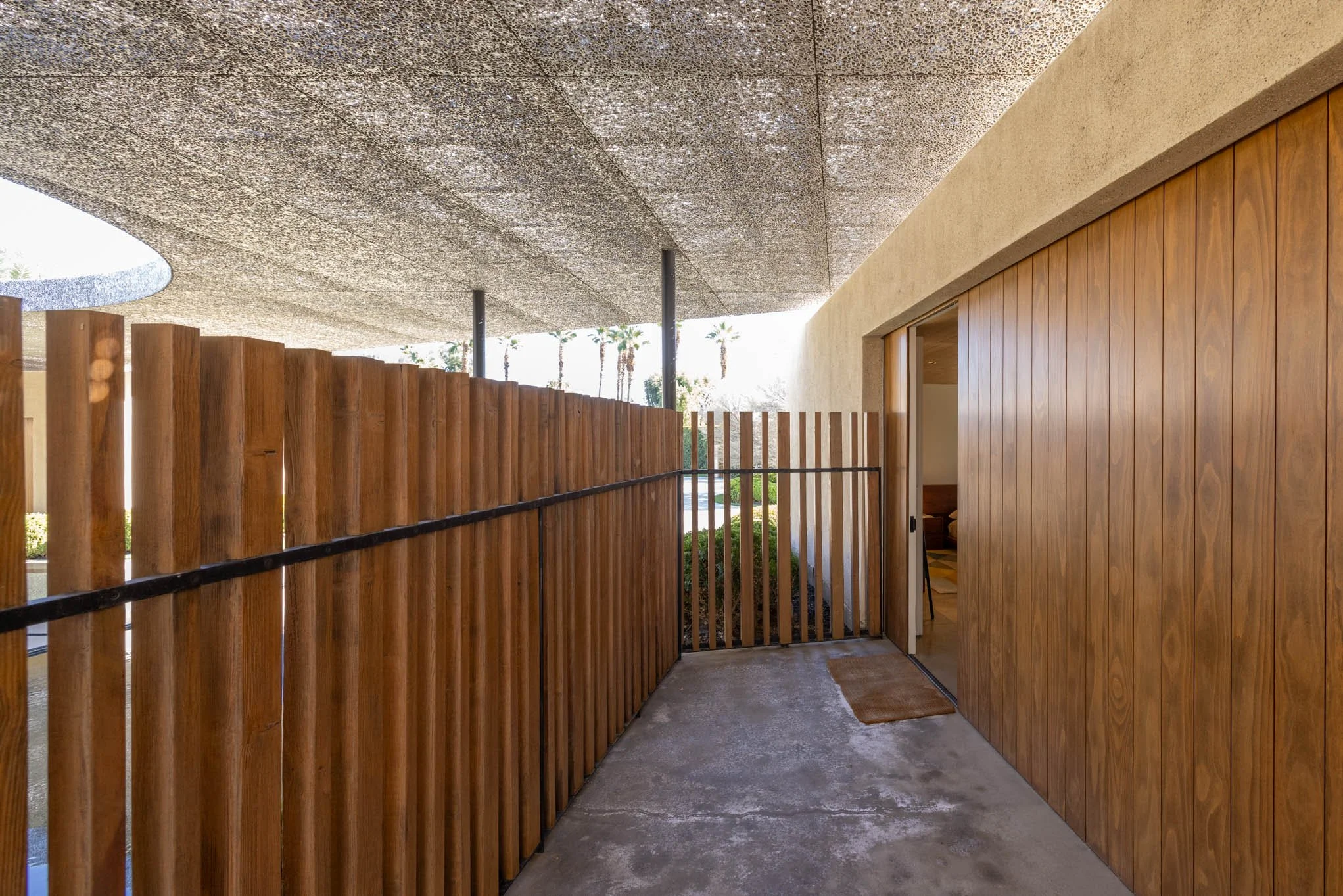 Outdoor patio with wooden fencing, concrete floor, and an open sliding door leading inside a house with wood paneling.