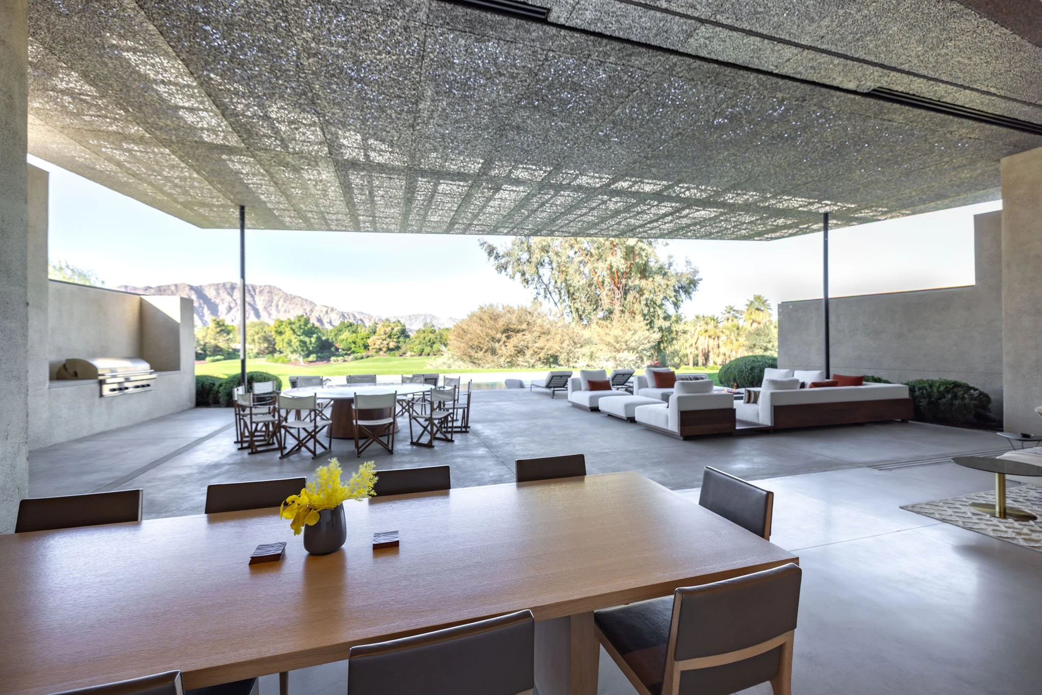 Open outdoor patio with white seating area, dining table with chairs, barbecue grill, and scenic mountain view in the background.