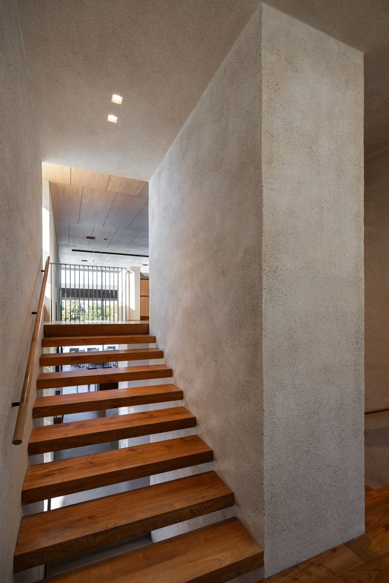 Interior view of a modern house with a wooden staircase, textured beige walls, and minimal lighting.