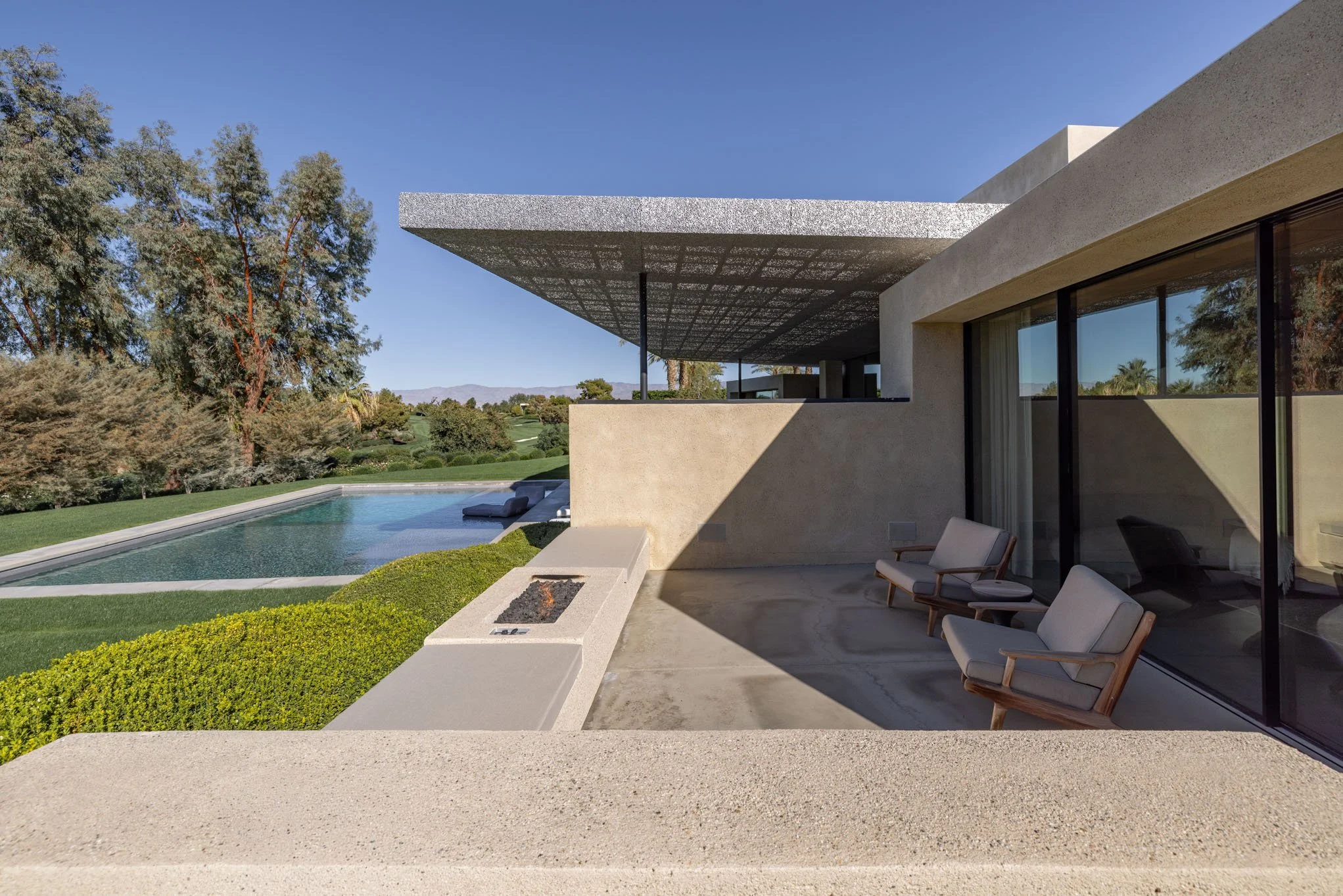 Luxury modern house patio with outdoor seating, nearby swimming pool, and scenic view of trees and mountains.