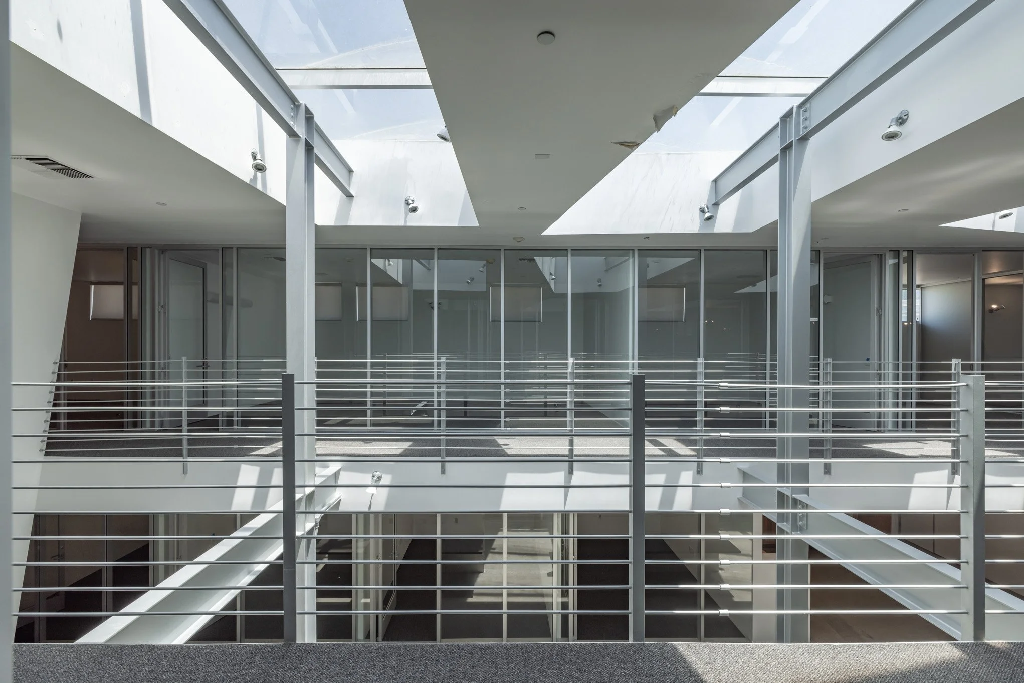 Interior view of a modern building with a glass ceiling and metal railings, showing multiple floors and an open atrium area.