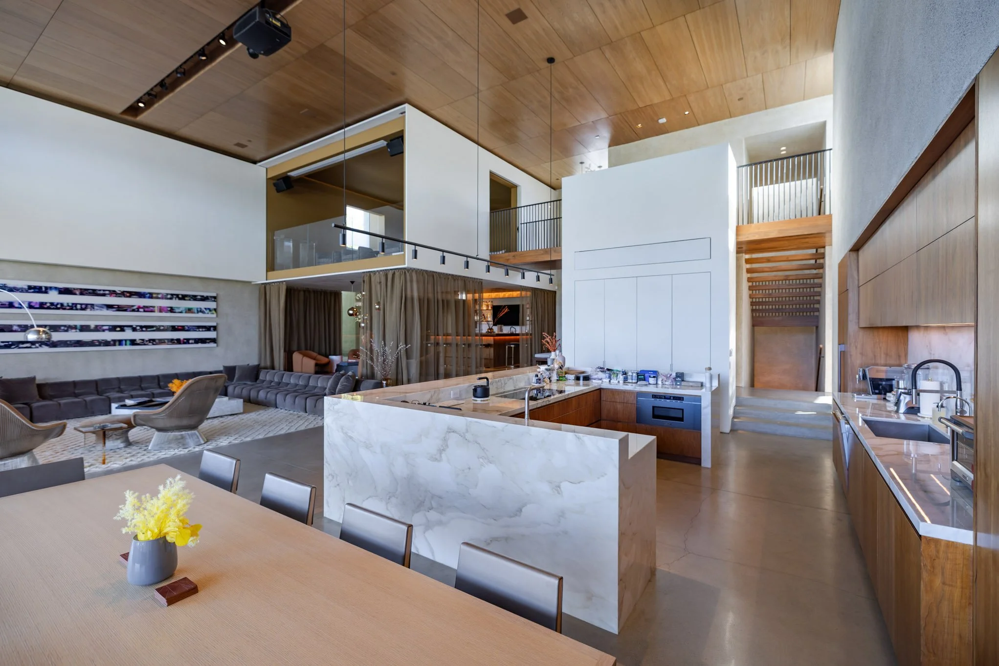 Open-concept modern living space with a kitchen, dining area, and living room, featuring a large marble island, wooden accents, and contemporary furniture.