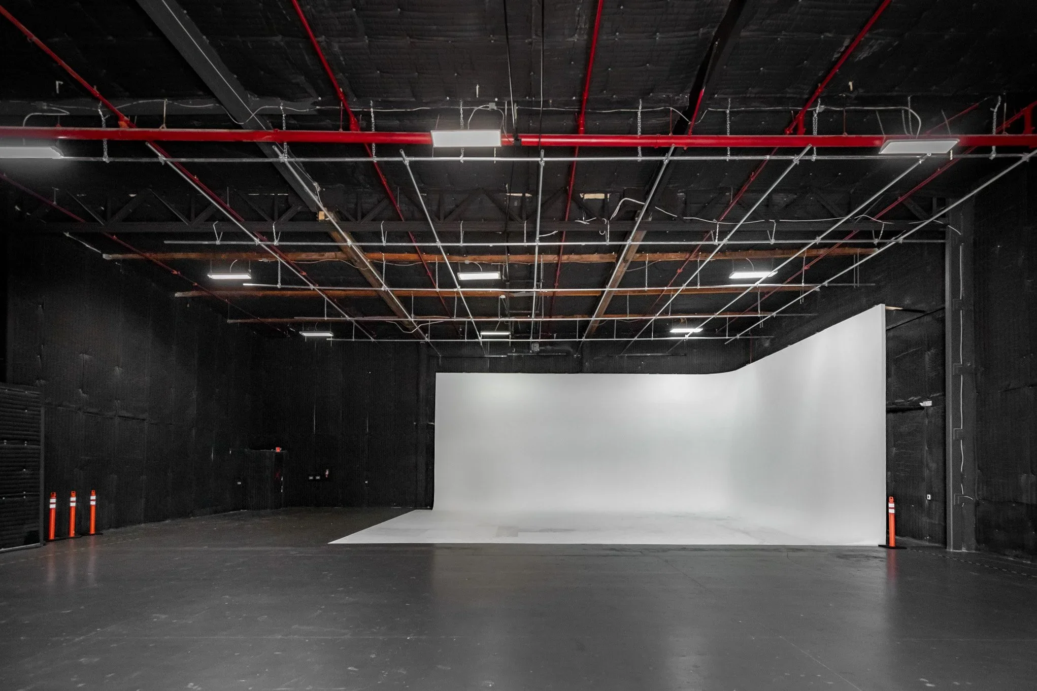 Empty black theater or studio space with a white projection screen, black walls, and ceiling, and red and white piping in the ceiling.