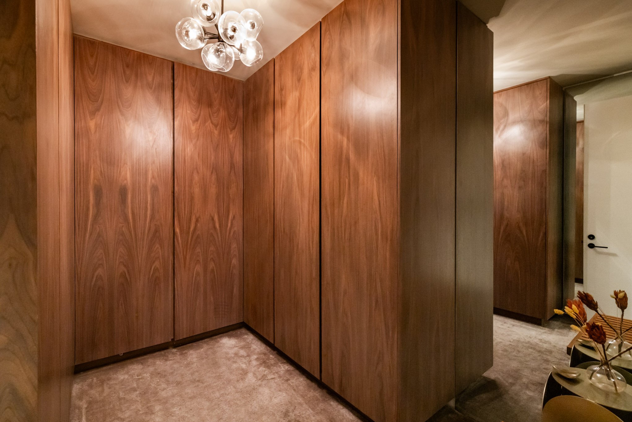 Wood-paneled walls and a beige carpeted floor in a hallway with a modern ceiling light fixture.