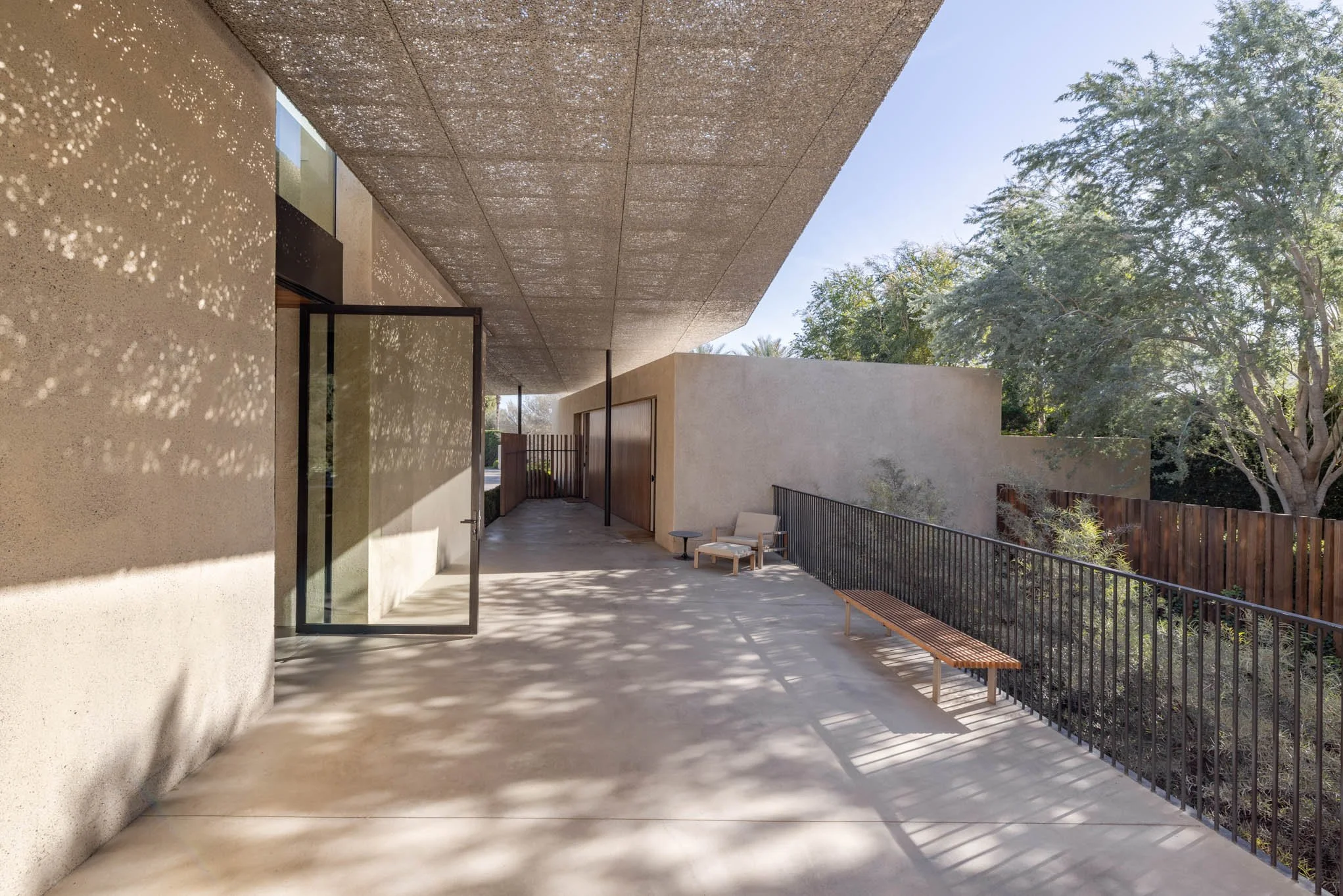 Modern outdoor patio with concrete flooring, metal and wood furniture, and a view of trees and a wooden fence.