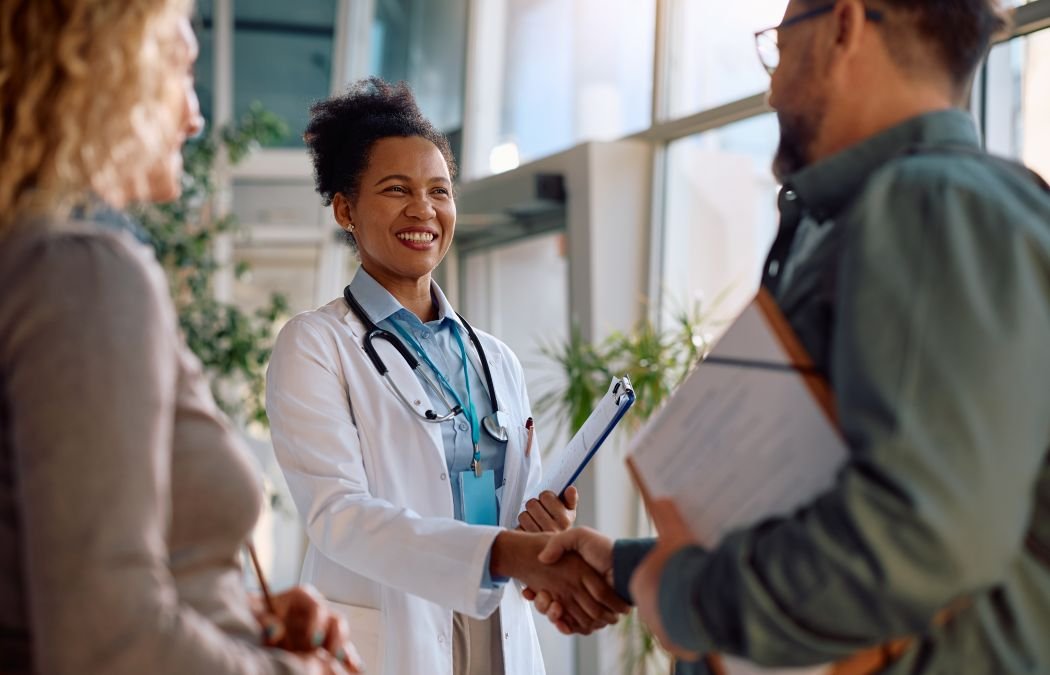 An Afro-American cheerful doctor welcoming a couple in a clinic reception