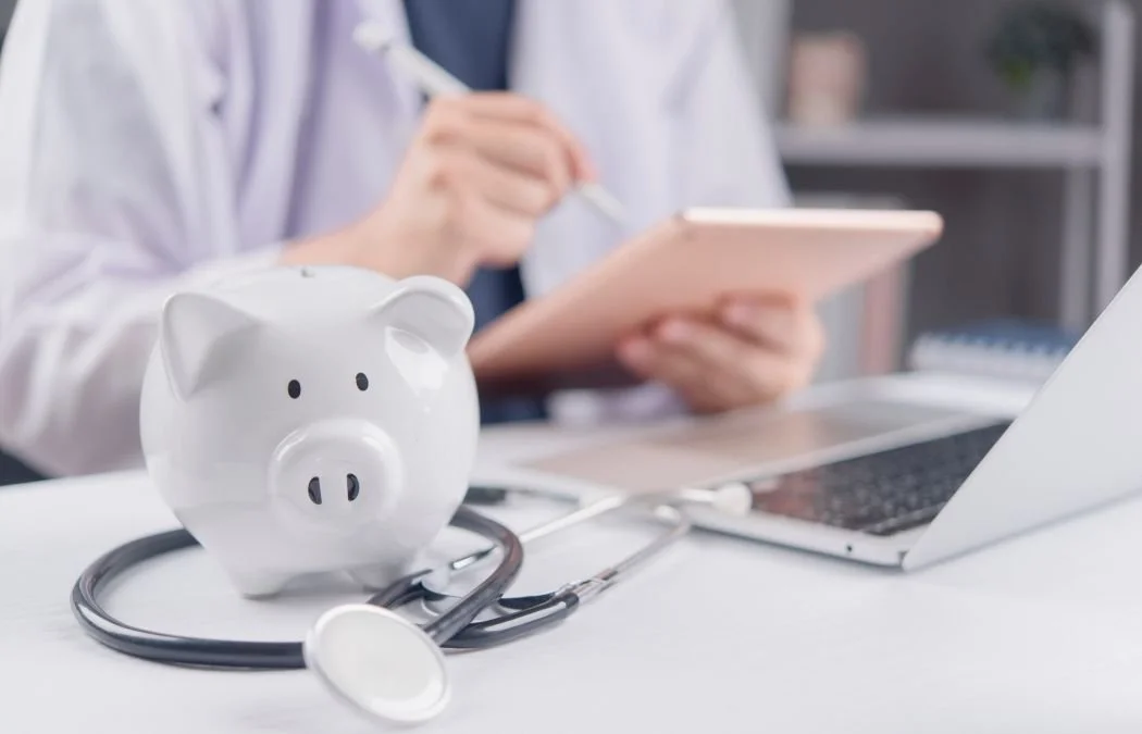 Piggy bank with stethoscope and doctor using tablet background.