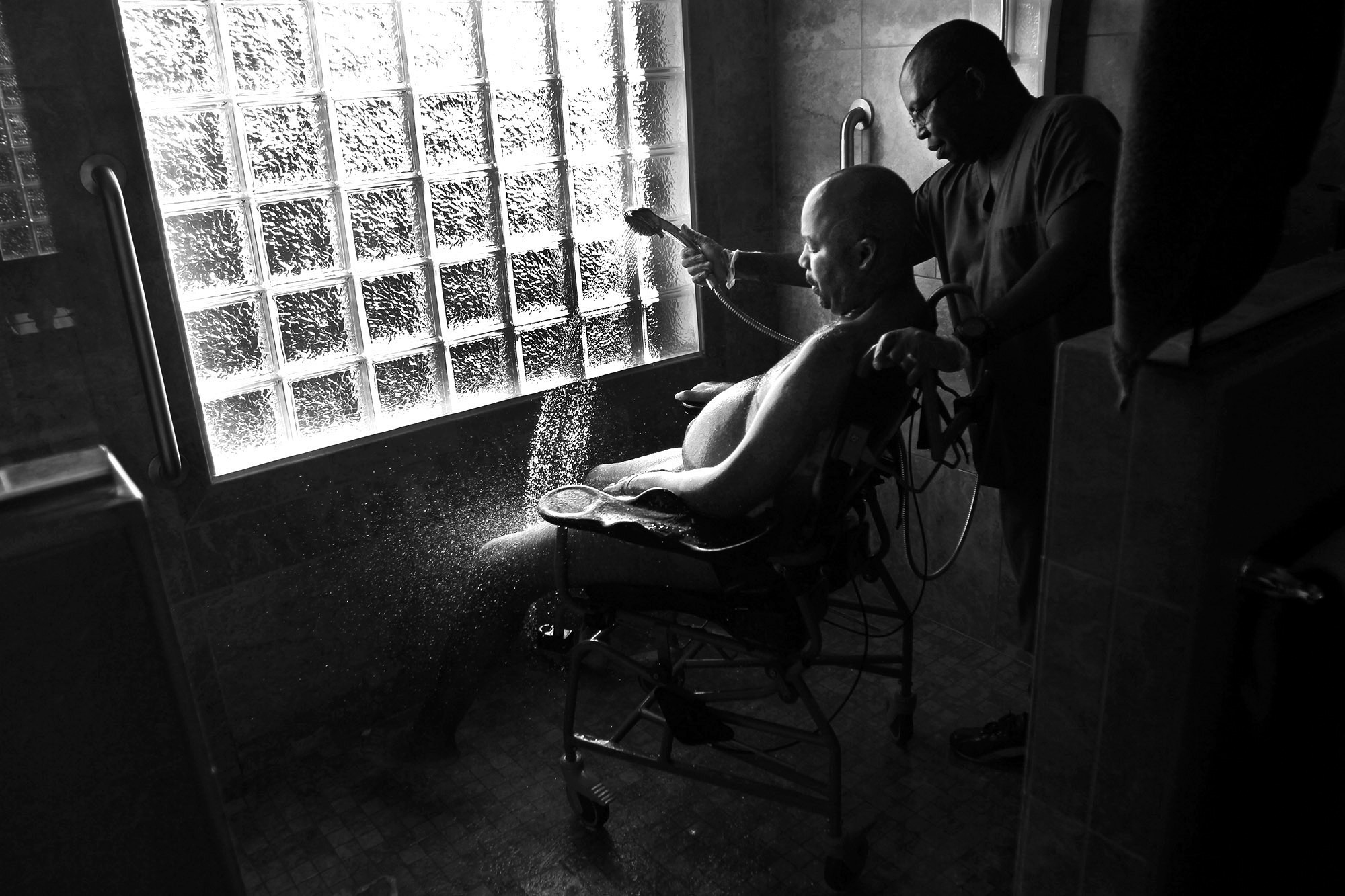  Professional caretaker James Ndegwa bathes Persian Gulf War veteran Mike White, who has amyotrophic lateral sclerosis, which renders him nearly paralyzed.&nbsp; 
