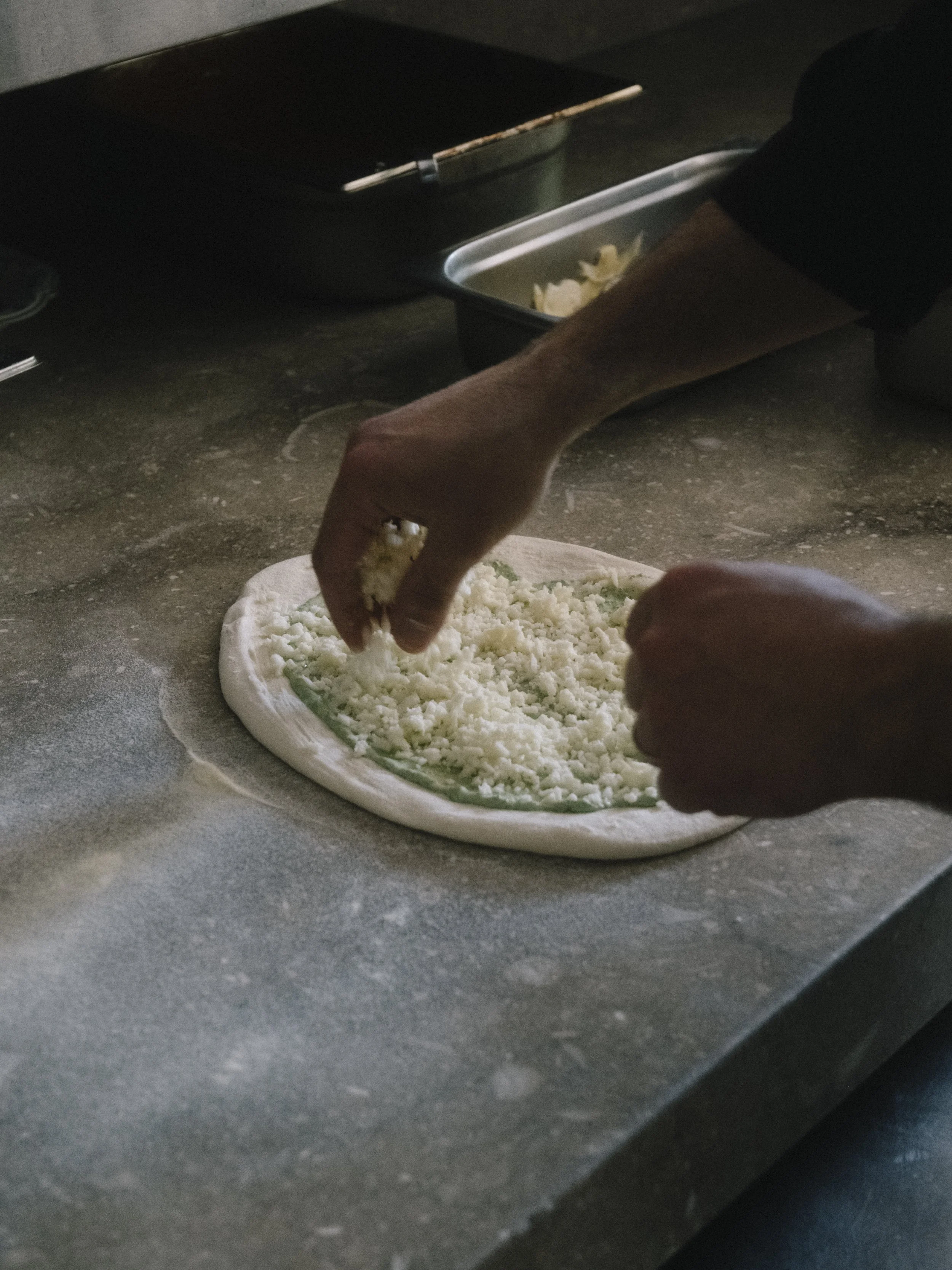 Elinde peynir serpeleyen kişinin görüldüğü bir pizza yapma süreci
