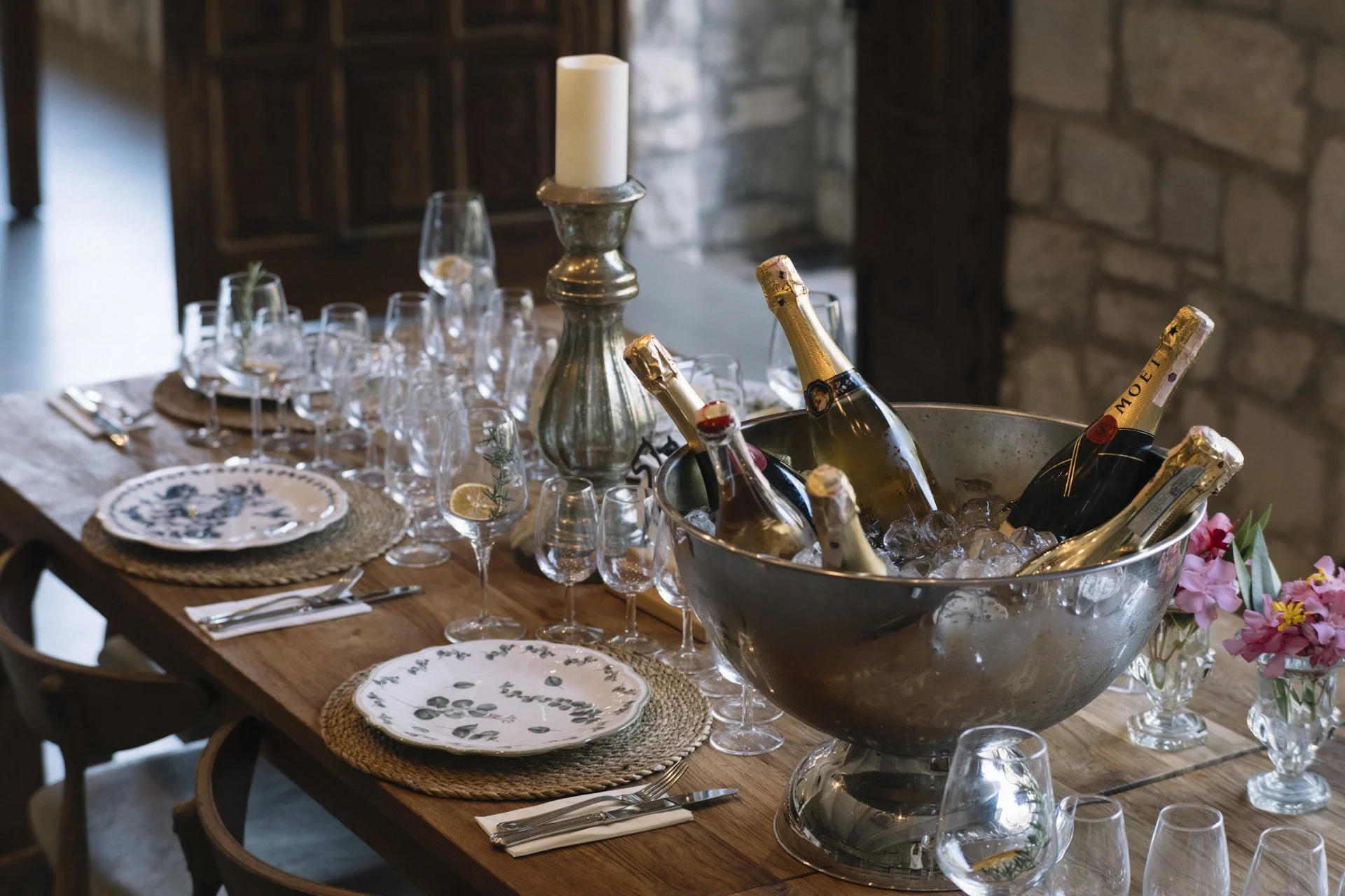 Bir masa pastel tonlarda tabaklar, cam bardaklar ve şampanya şişeleri ile süslenmiş; ortasında büyük bir buzluk var.