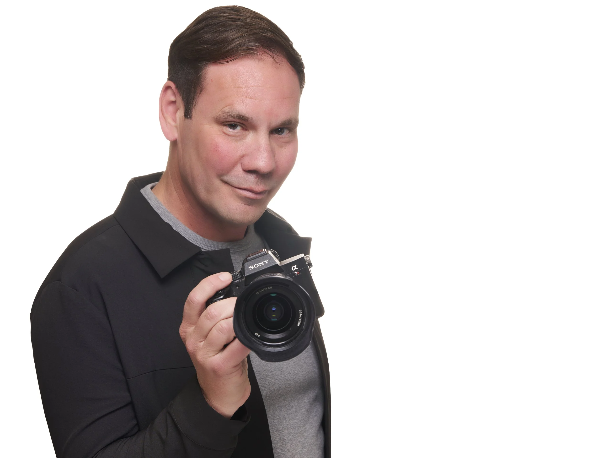 Jason in front of white studio background holding his camera in Pacific Grove studio