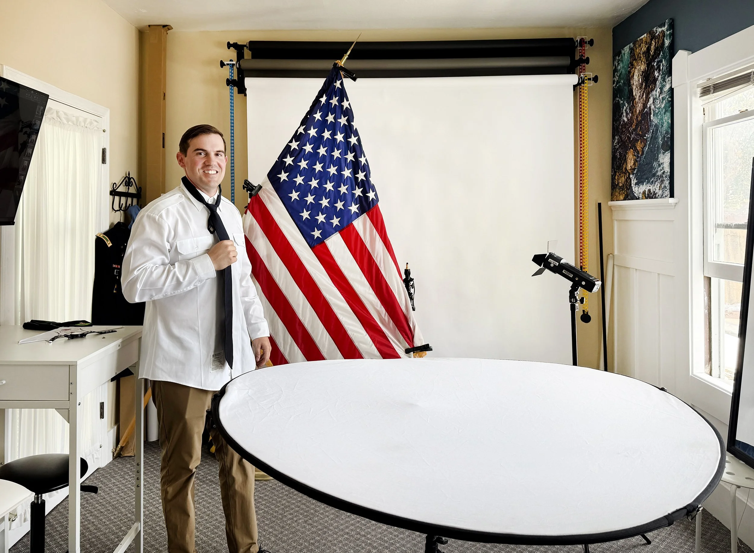 Behind the scenes of military headshot session showing lighting setup, reflector, and American flag positioned in small studio space