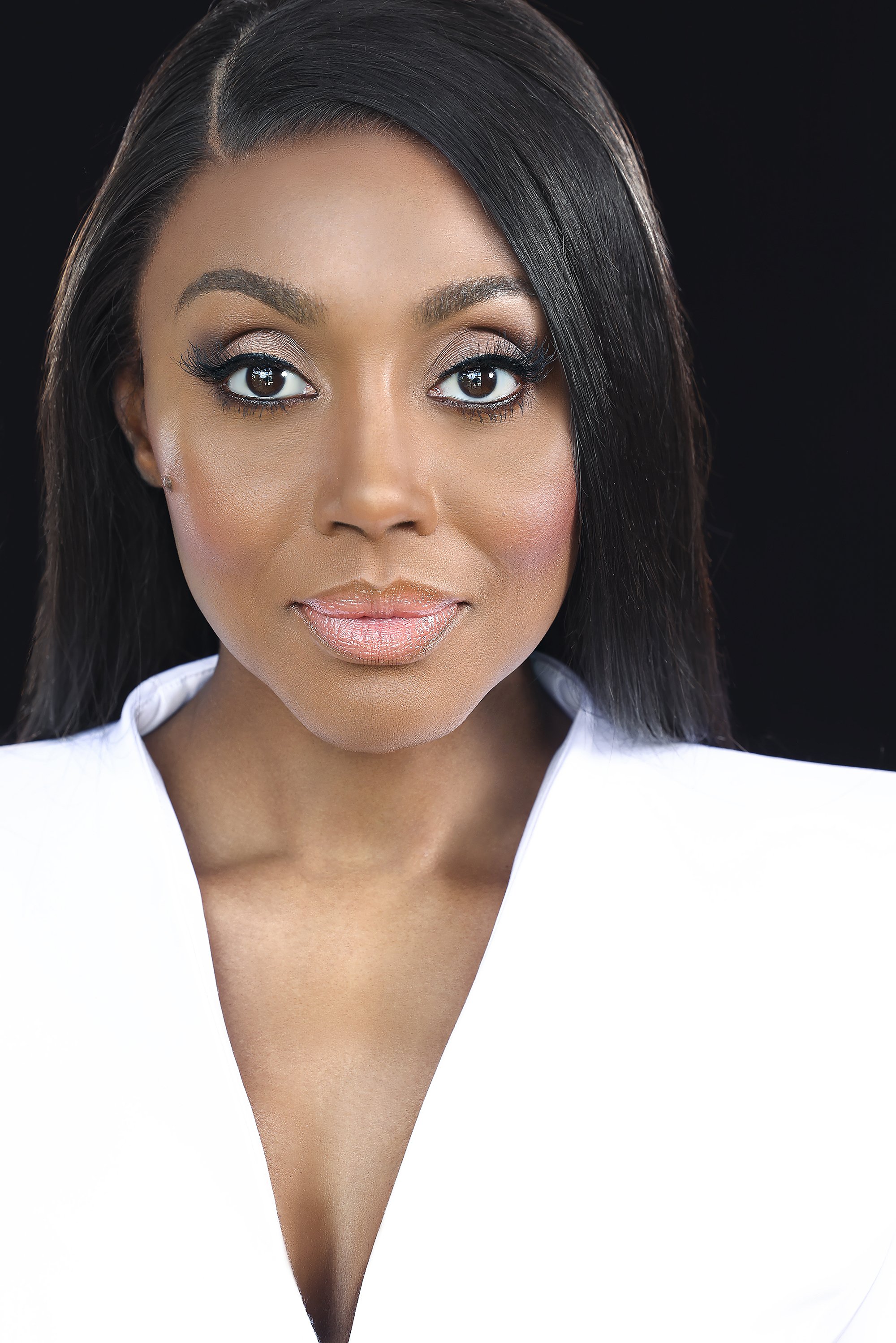 Close-up portrait of a woman with dark hair, makeup, and wearing a white top against a black background. Photography by Kenneth Dolin, top Los Angeles headshot photographer. 