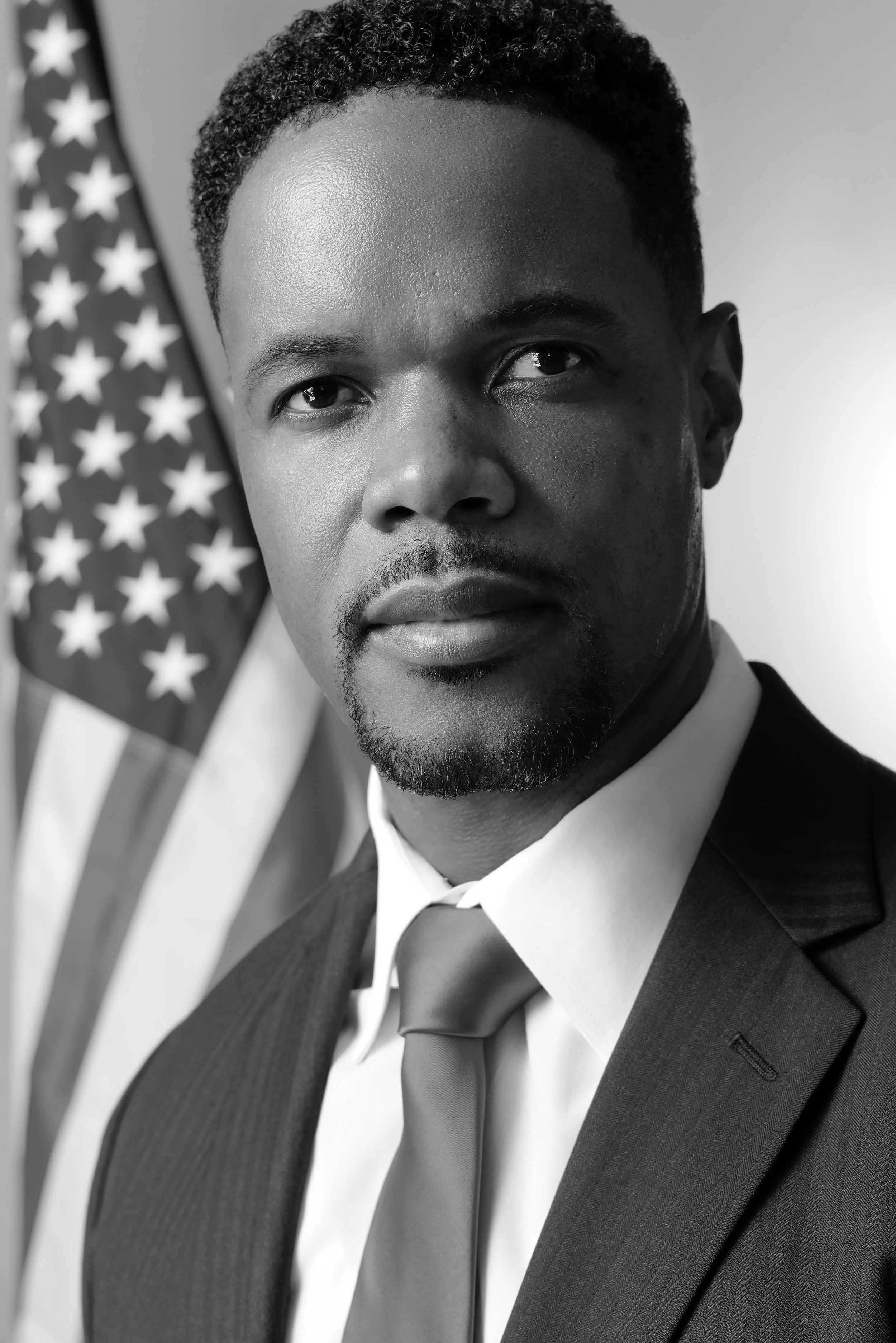 Black man in a suit and tie in front of an American flag