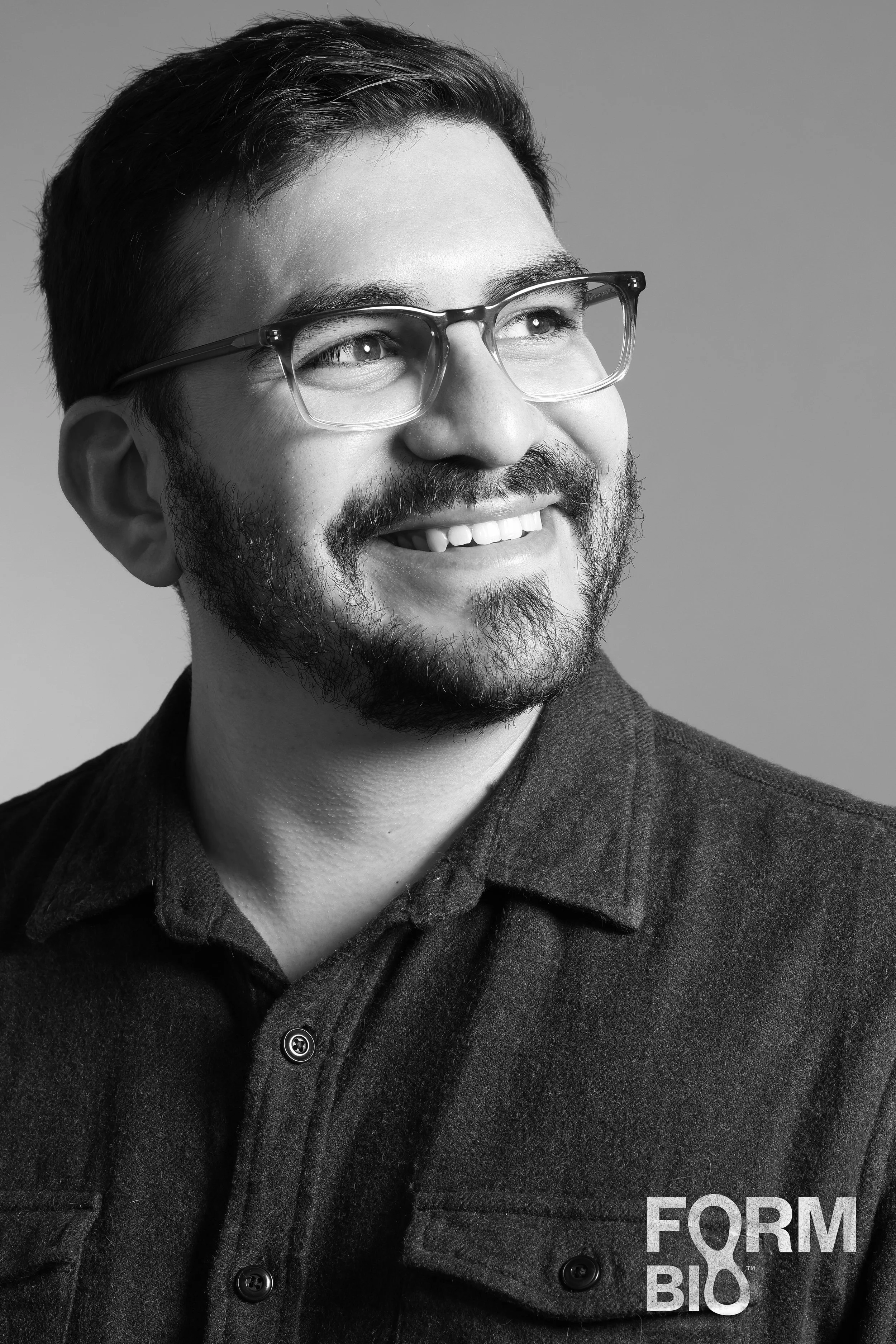 A smiling man with glasses and a beard, wearing a dark shirt, looking to the right. The photo is black and white and includes the logo 'FORM BIO' in the bottom right corner.