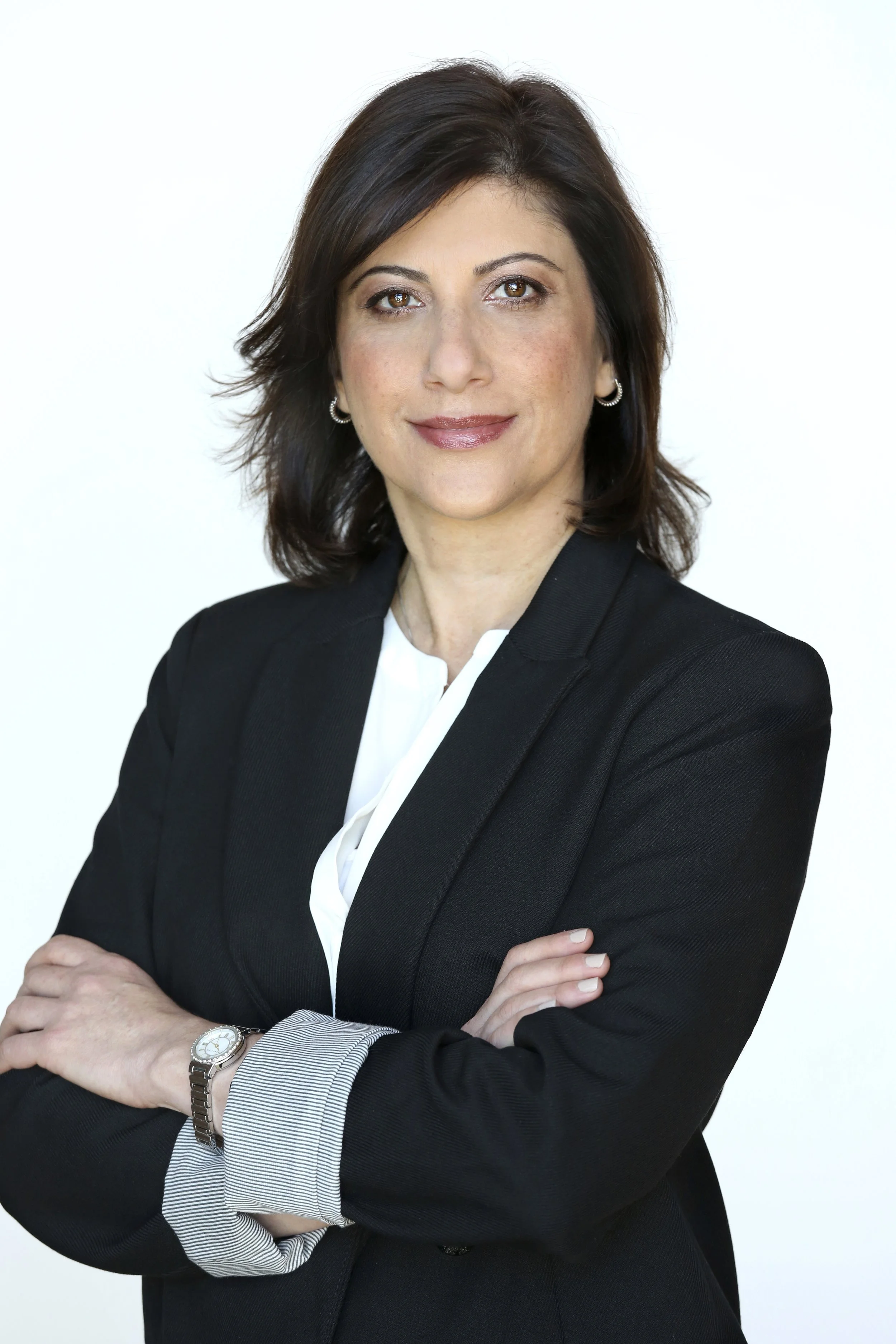 Professional woman with brown hair wearing a black blazer and white shirt, arms crossed, standing against a white background