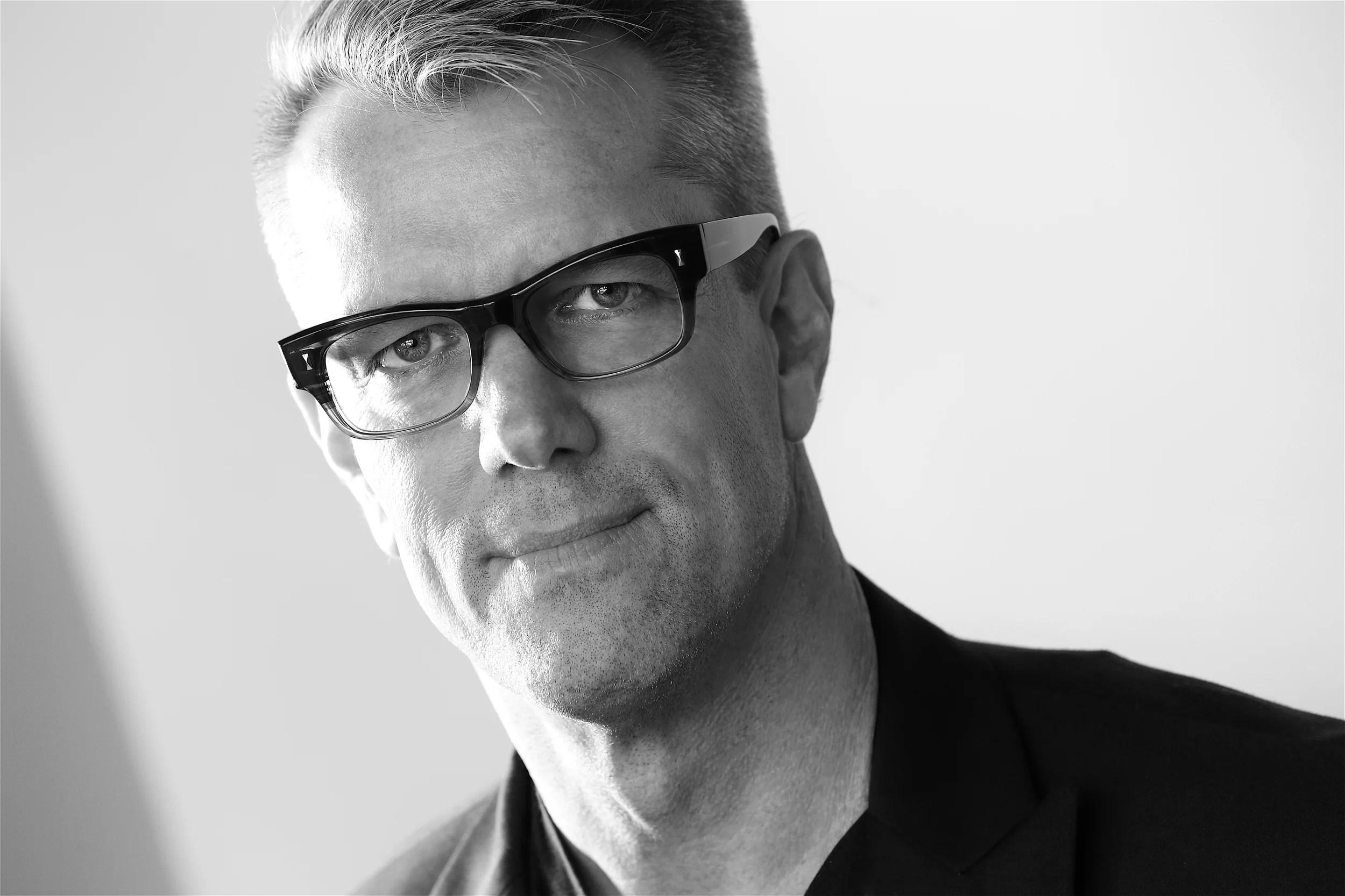 Black and white portrait of a man with light-colored hair, wearing glasses and a dark suit, looking directly at the camera with a slight smile. Photography by Kenneth Dolin, top Los Angeles headshot photographer. 
