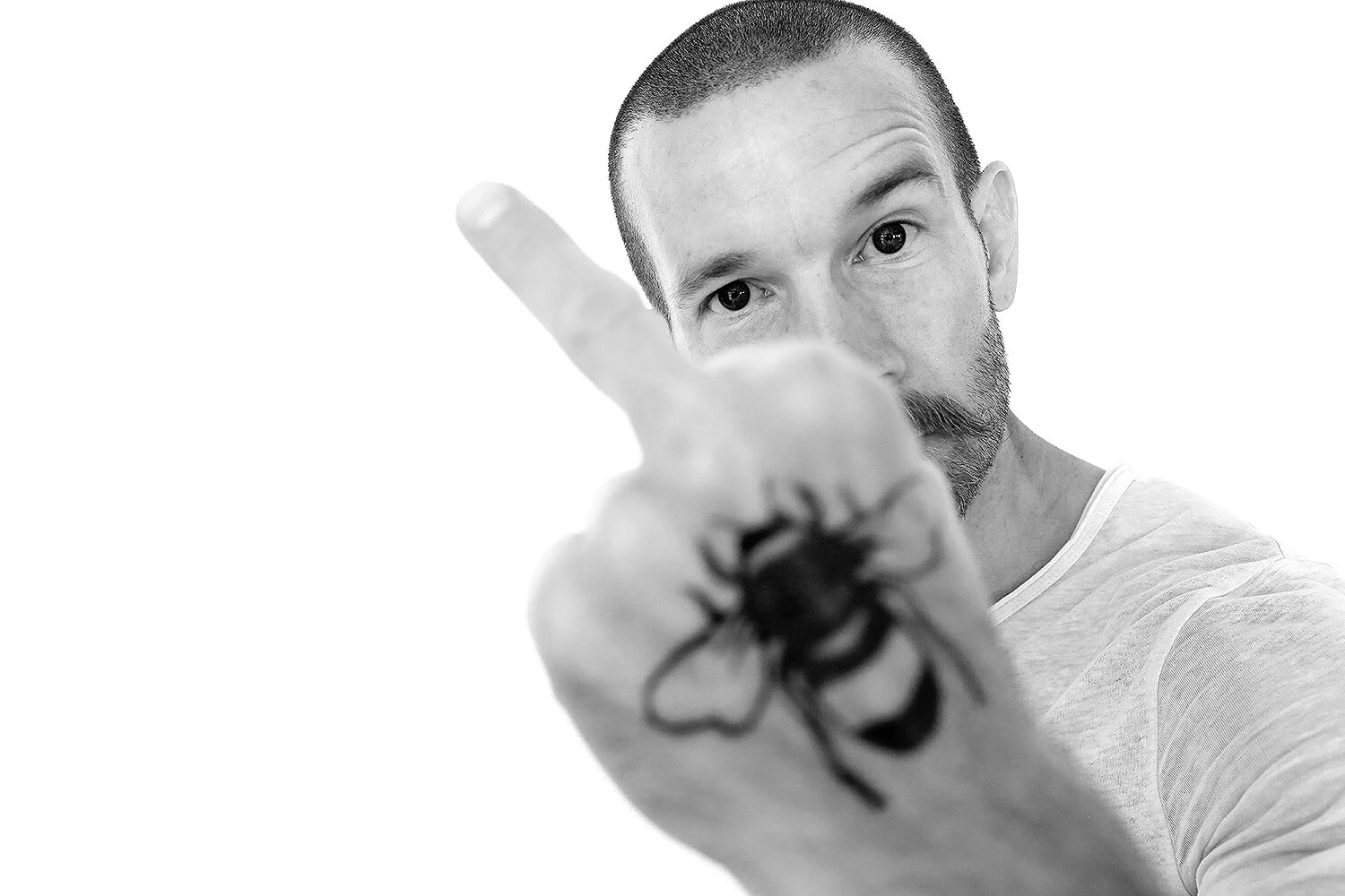 Black and white photo of a man with a tattoo on his hand, pointing his finger towards the camera and looking directly.