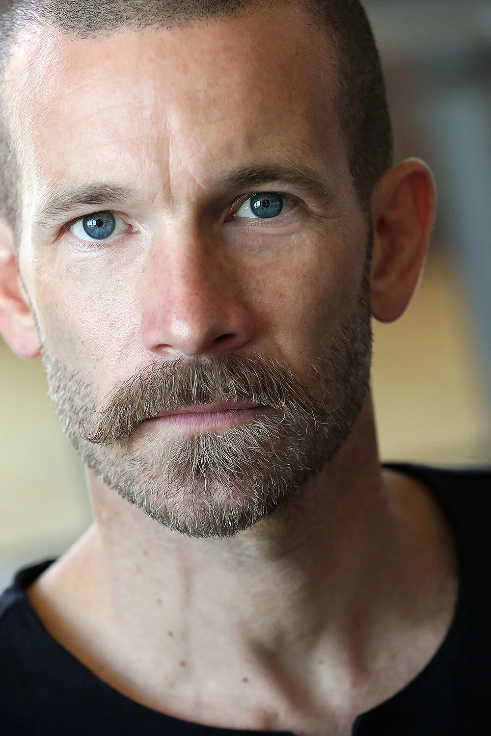 Close-up of a man with blue eyes, short hair, beard, and mustache looking into the camera.