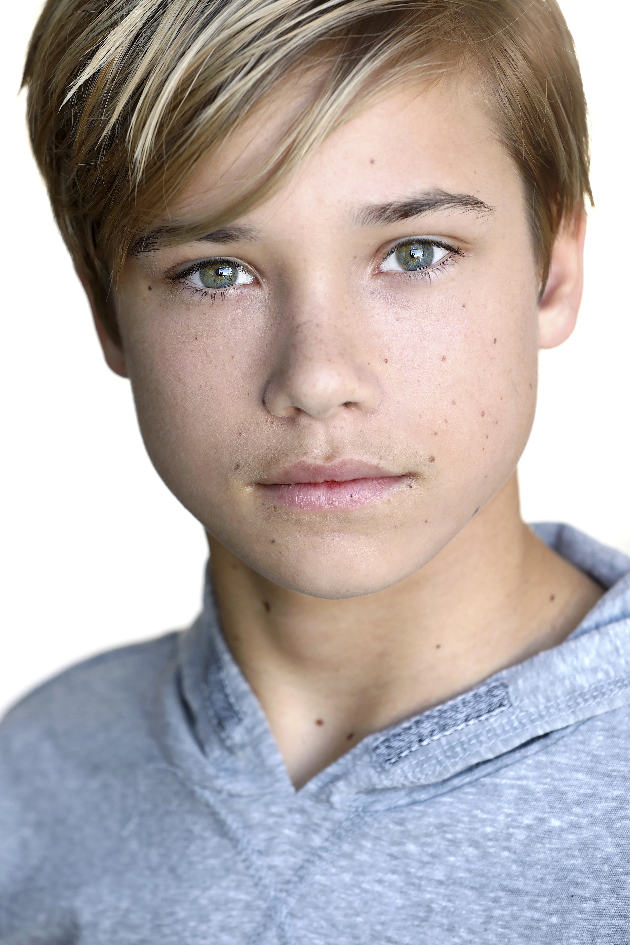 Close-up portrait of a young boy with blue eyes, light freckles, and short, blonde hair wearing a gray hoodie.