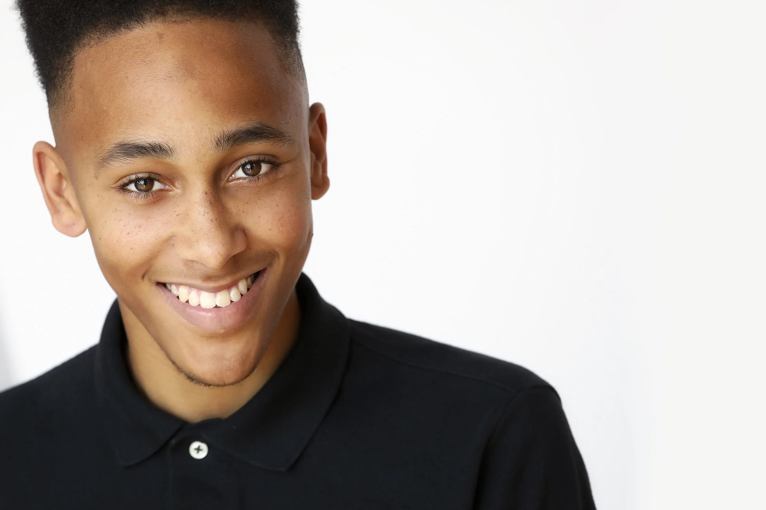 Smiling young man with short hair, freckles, and a black polo shirt against a white background.