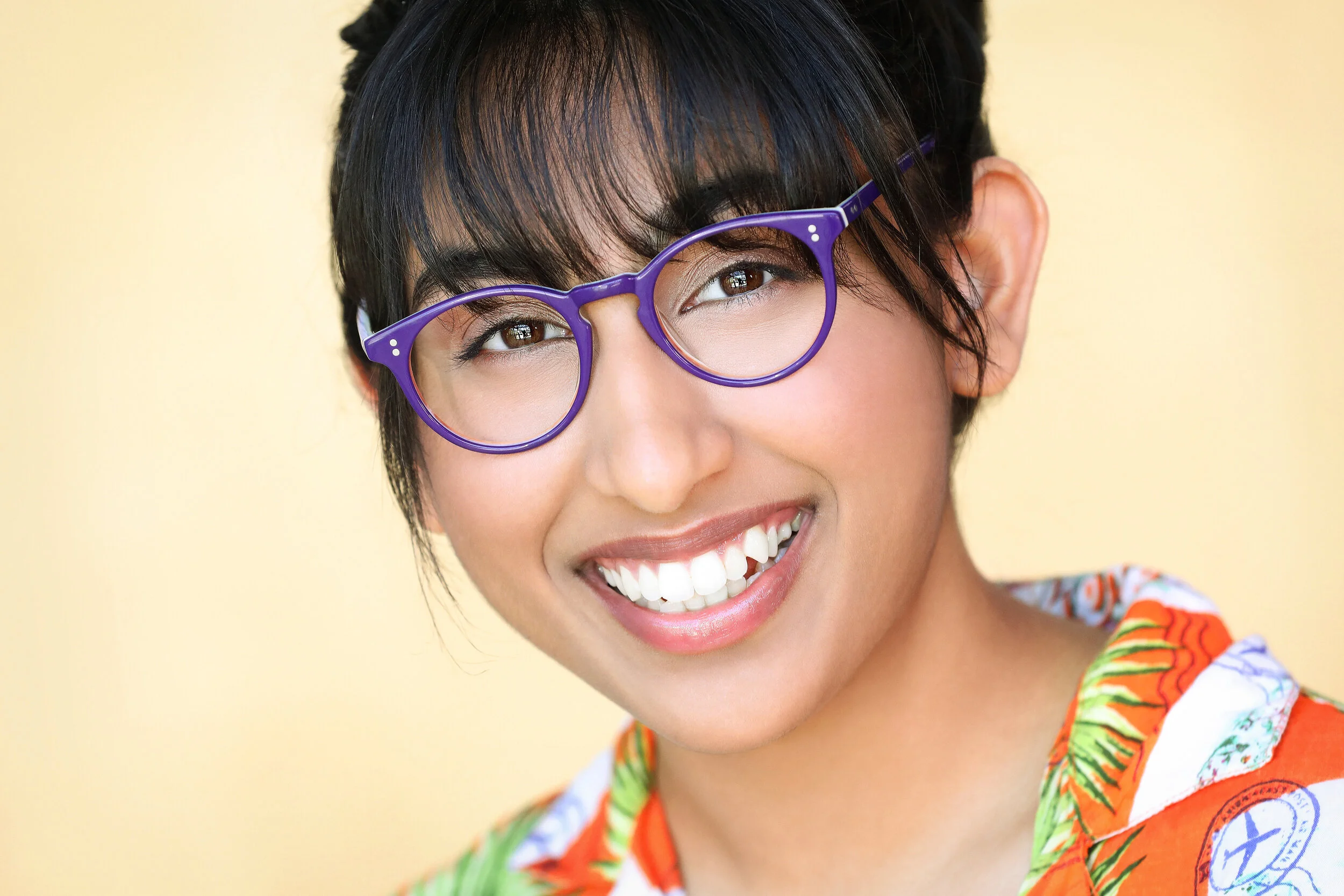 Person with short dark hair, wearing purple glasses and a colorful tropical-patterned shirt, smiling at the camera.