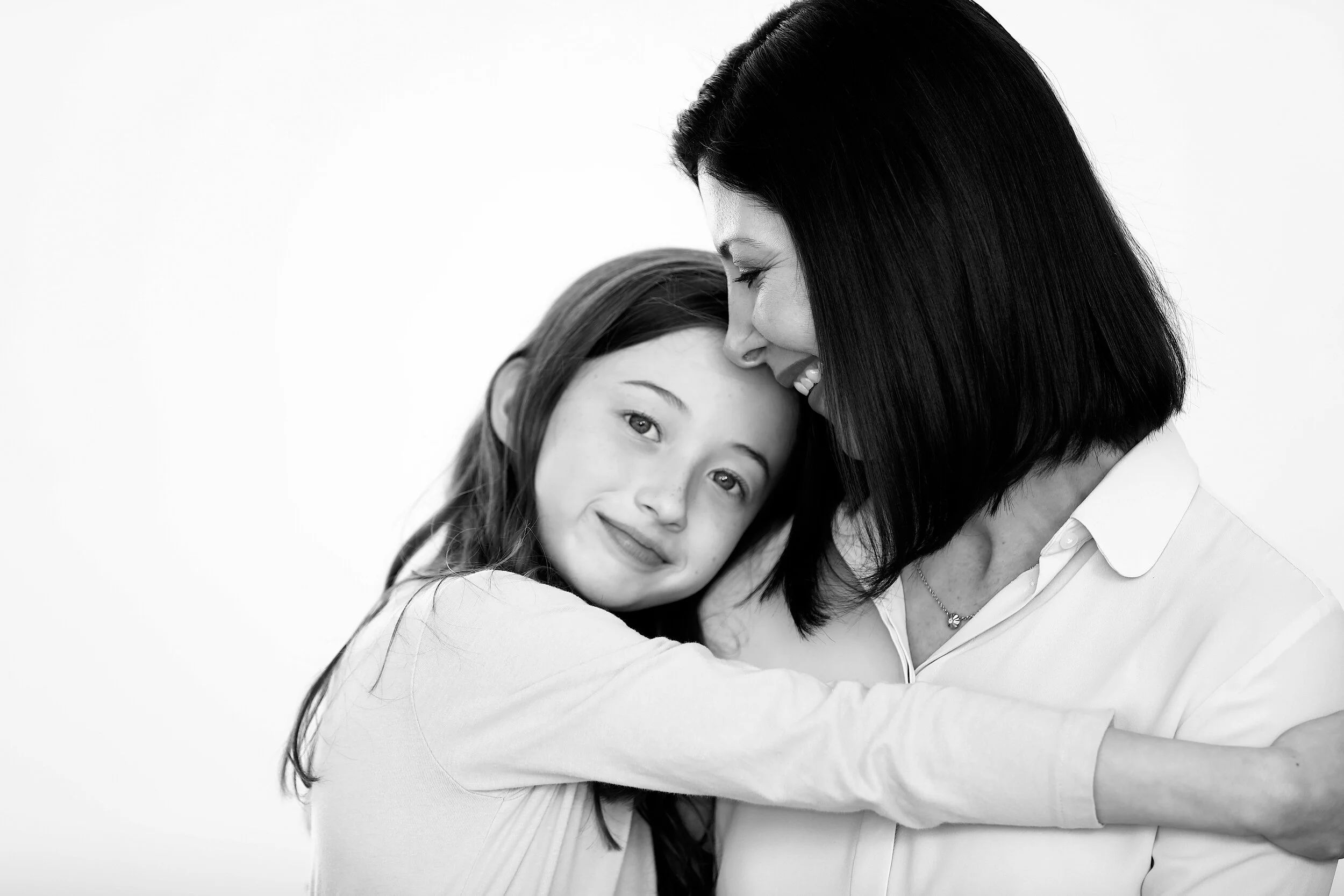 A woman and a girl embrace, smiling affectionately at each other in a black and white portrait.
