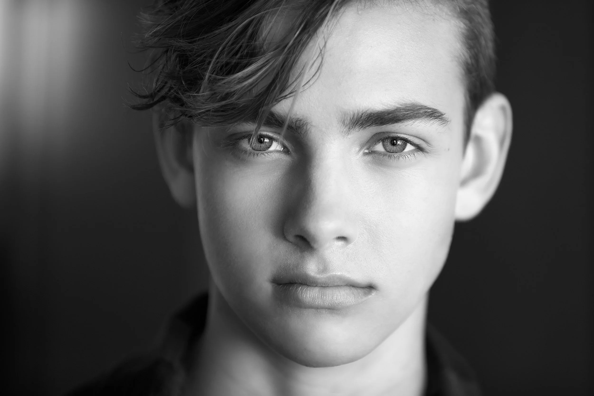 Black and white close-up portrait of a young person with short, wavy hair and piercing eyes.