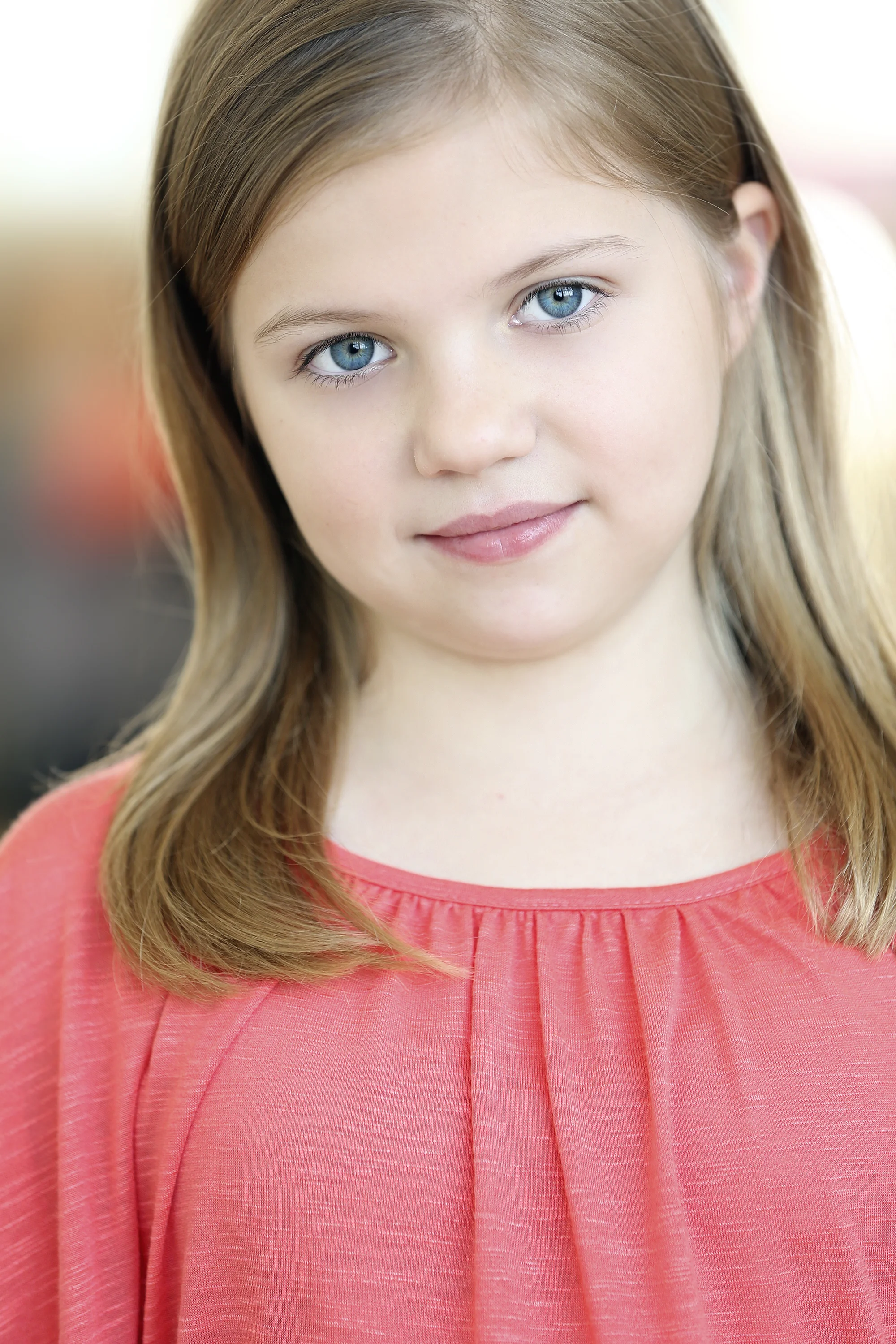 Close-up of a young girl with blue eyes and light brown hair wearing a coral-colored top.