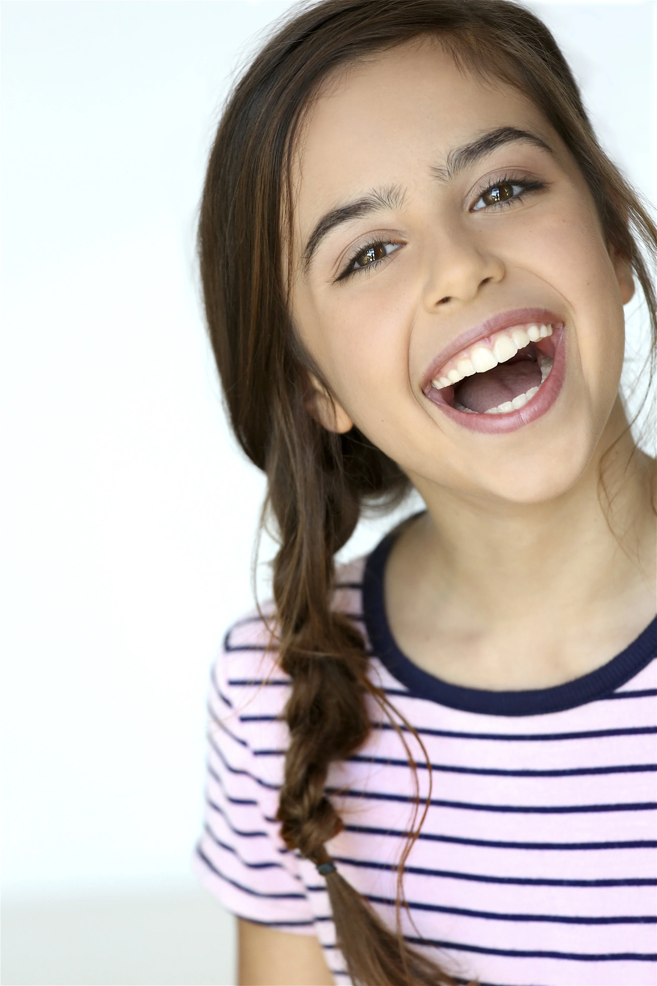 Close-up of a smiling young girl with long brown hair in a braid, wearing a pink and black striped shirt.