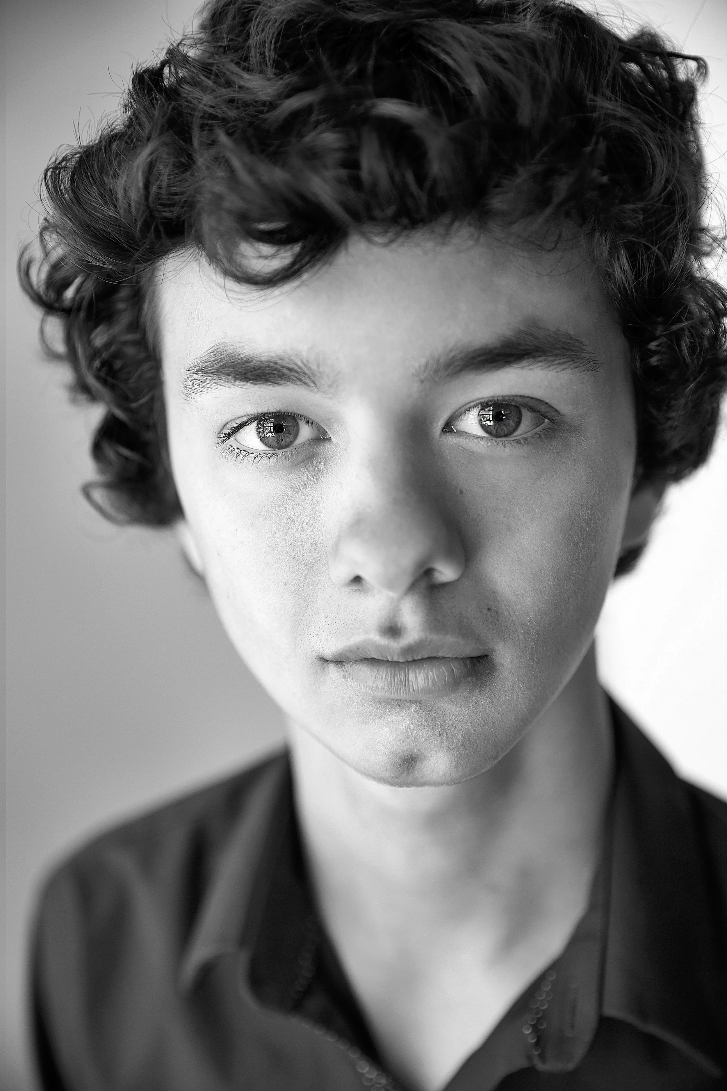Close-up black and white portrait of a young person with curly hair and light skin, wearing a dark shirt.