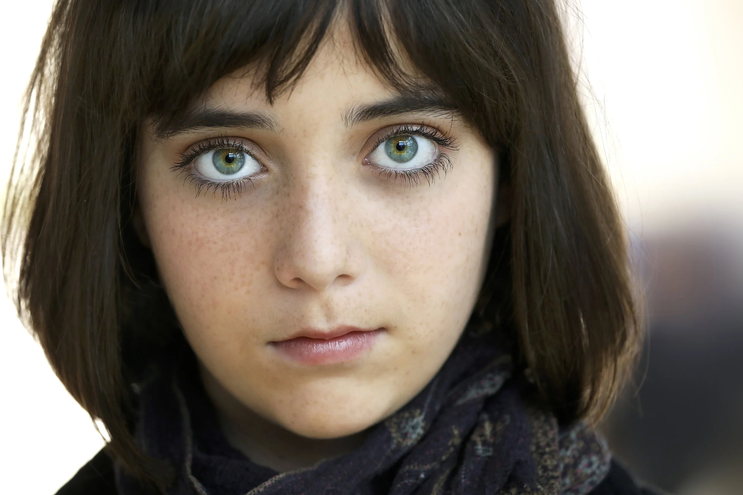 A young woman with blue eyes, dark brown hair, freckles, and a dark scarf around her neck.