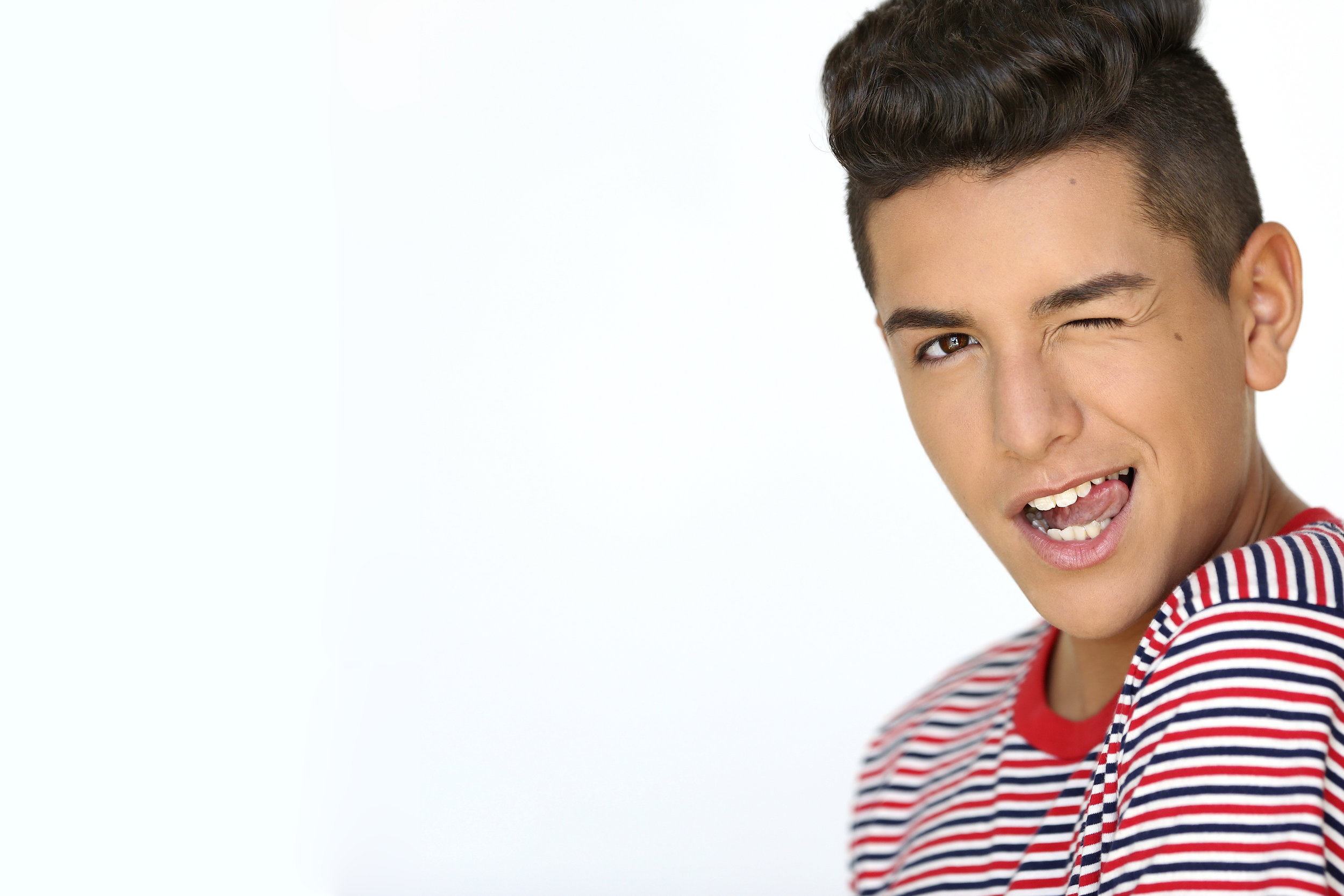 Young boy with short dark hair winking, sticking out tongue, and wearing a red, white, and blue striped shirt.