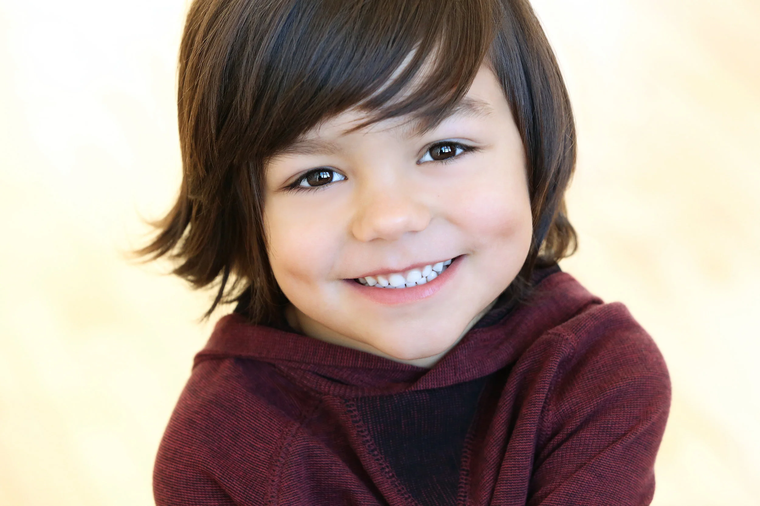 Close-up of a smiling young boy with brown hair wearing a maroon hoodie.