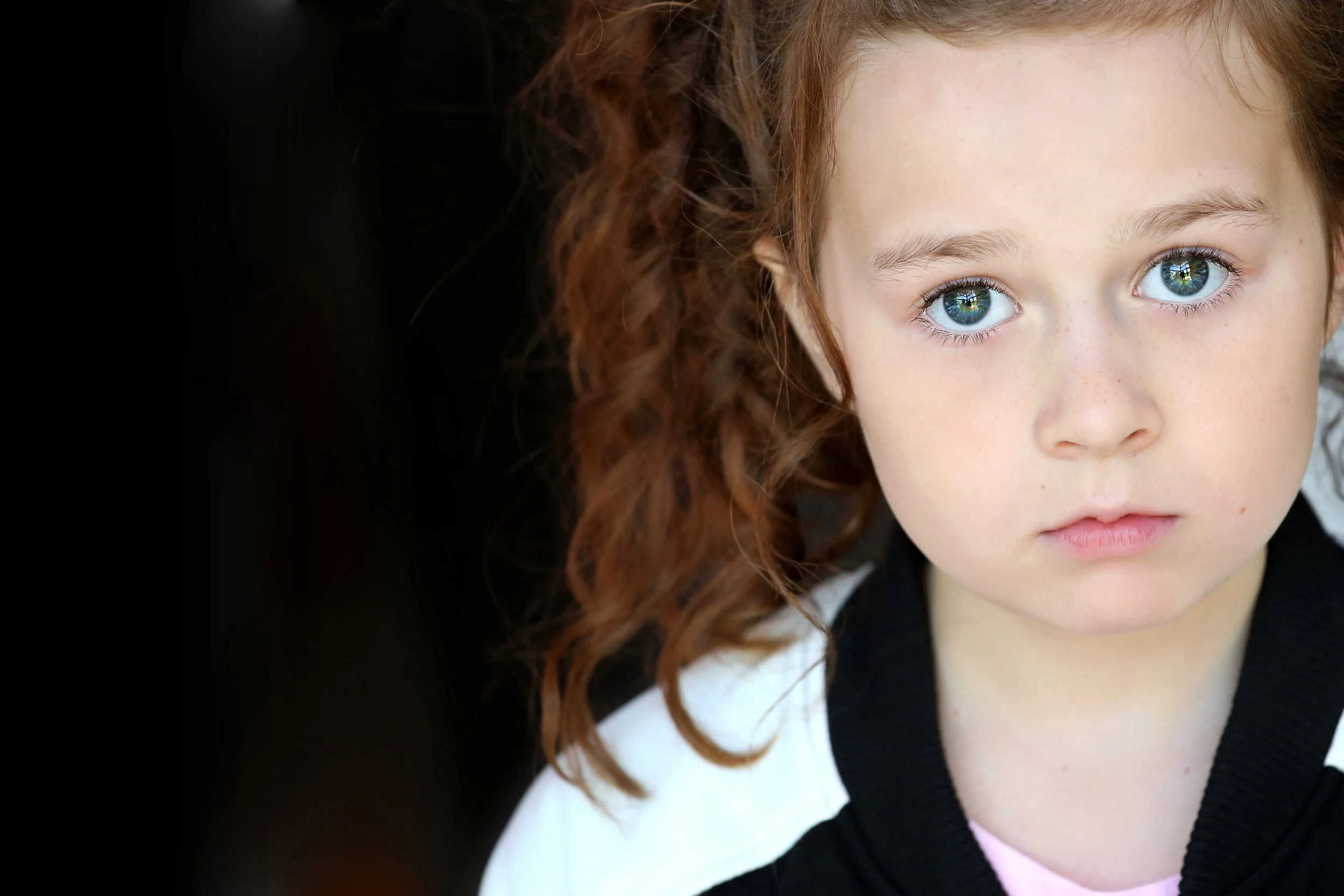 Close-up of a young girl with curly red hair and blue eyes, looking directly at the camera.