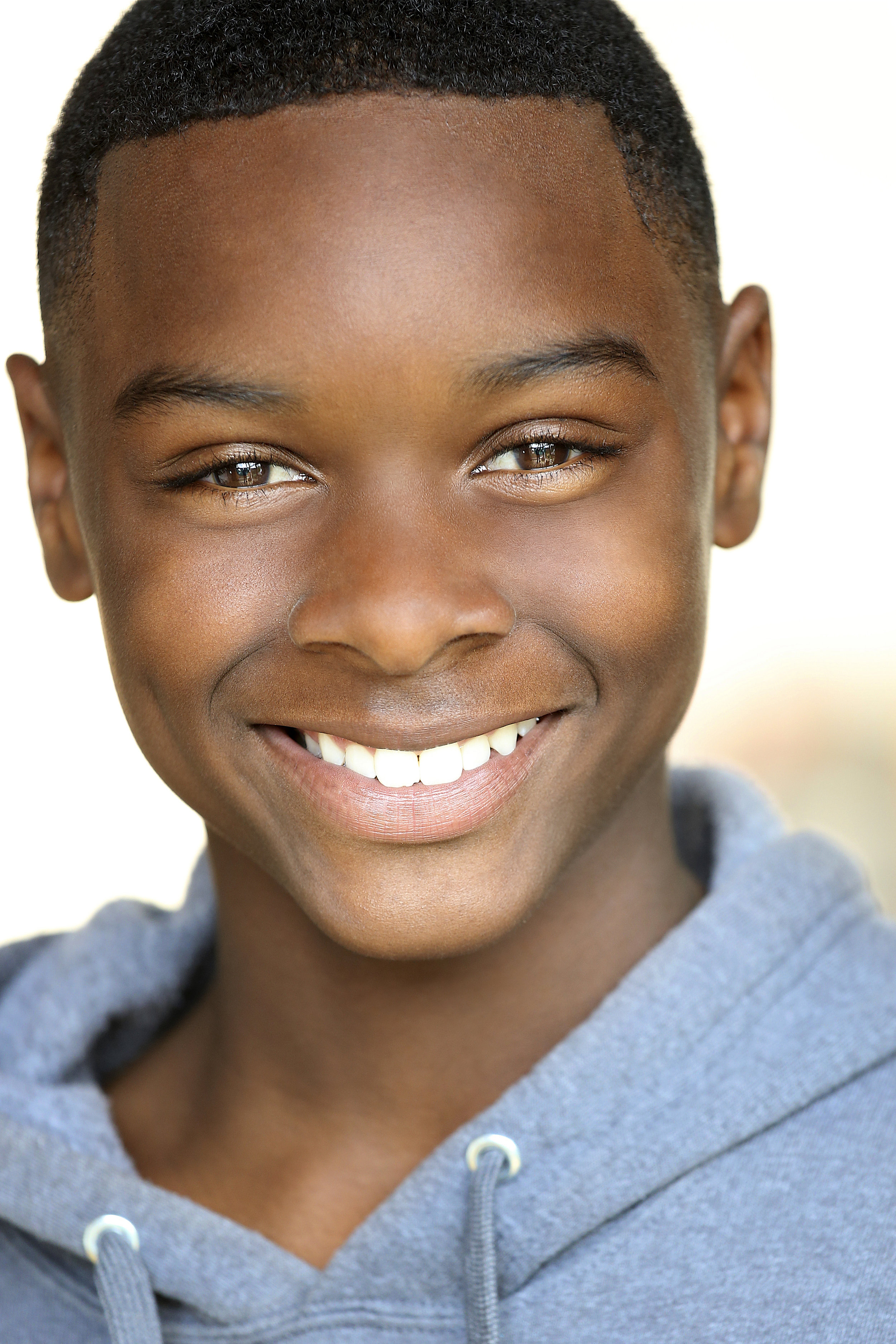 Close-up of a smiling young African American boy wearing a gray hoodie.