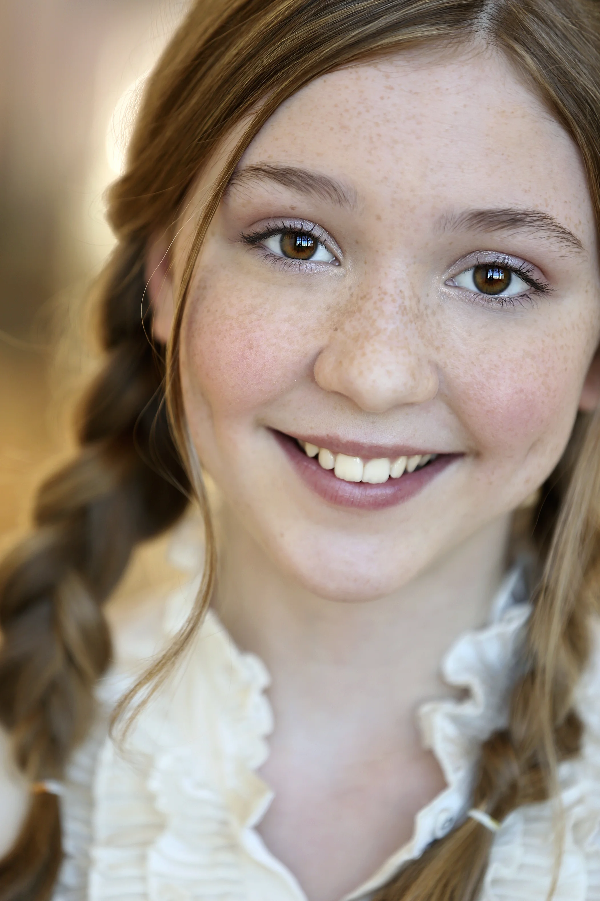 Close-up of a smiling young red-haired girl with freckles, brown eyes, and braided hair, wearing a ruffled white blouse.