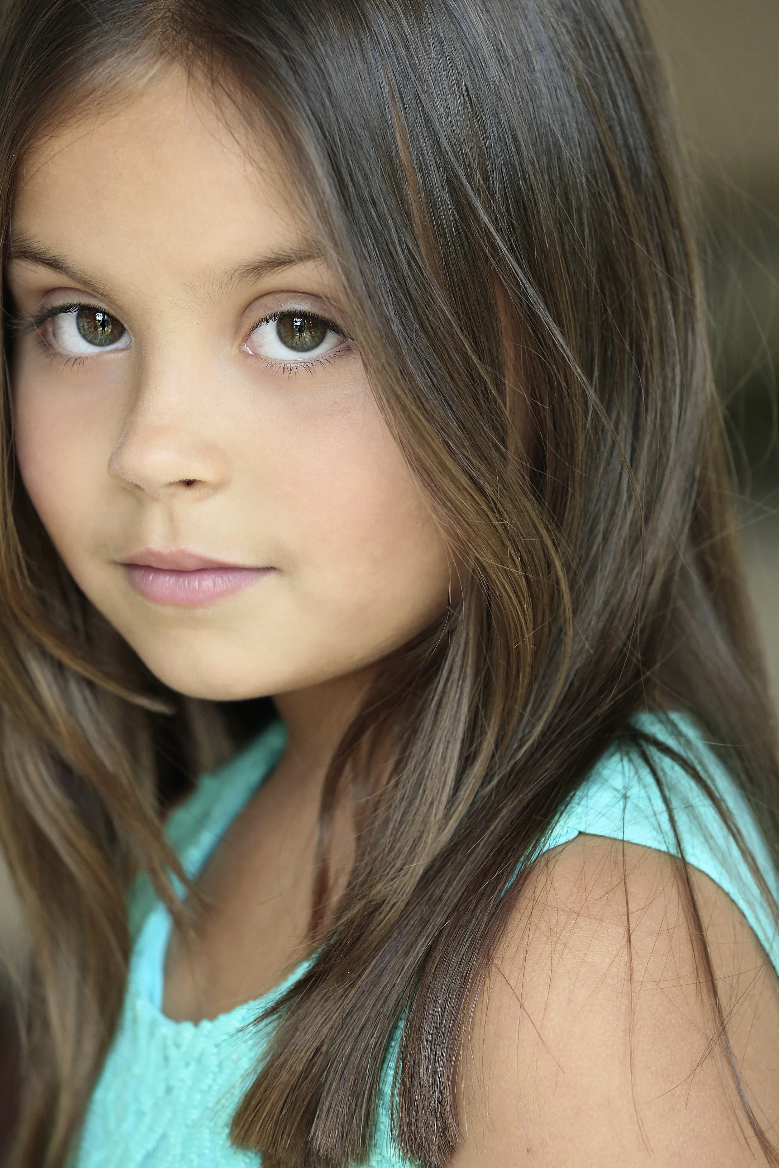 Close-up of a young girl with long brown hair and hazel eyes wearing a turquoise top.