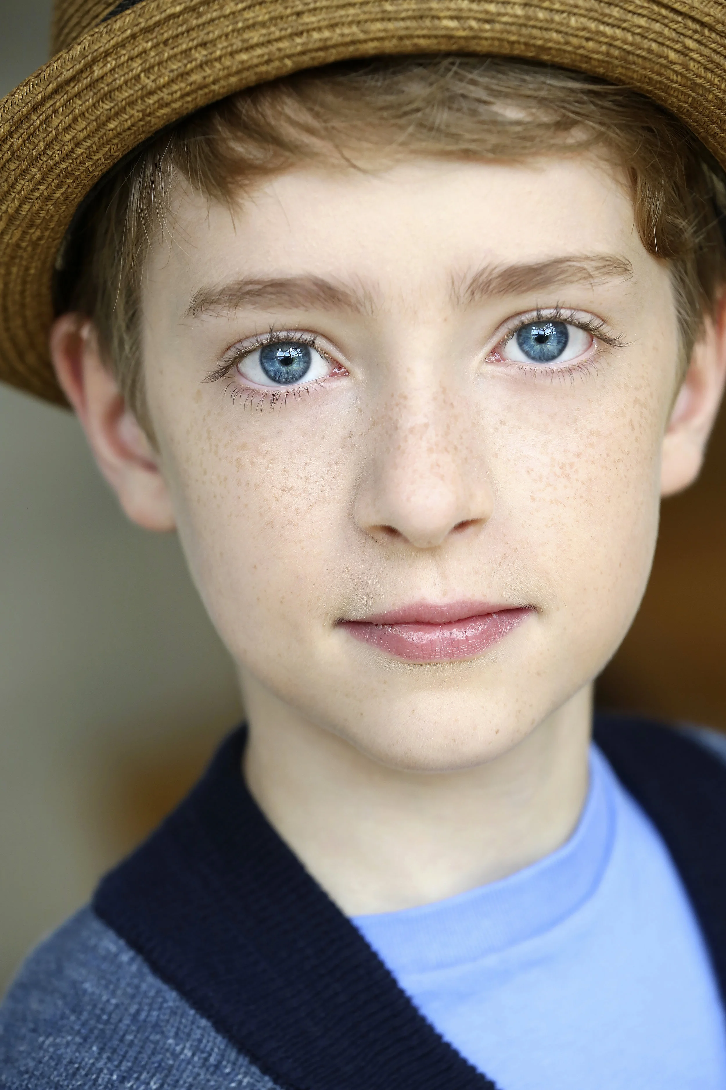 Close-up of a young boy with blue eyes, freckles, wearing a straw hat and a blue shirt.