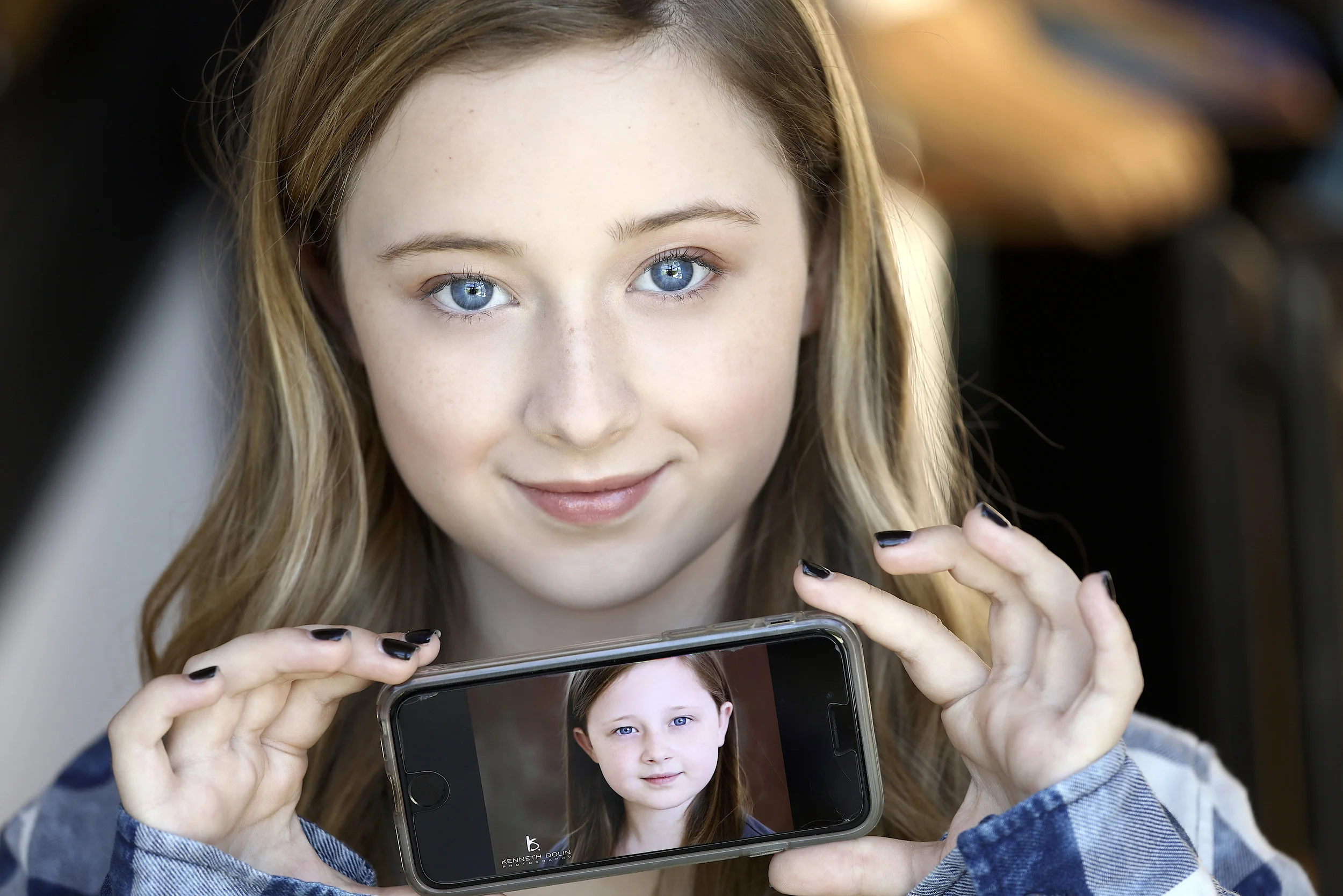 A young girl with blue eyes and light brown hair taking a selfie with her smartphone.