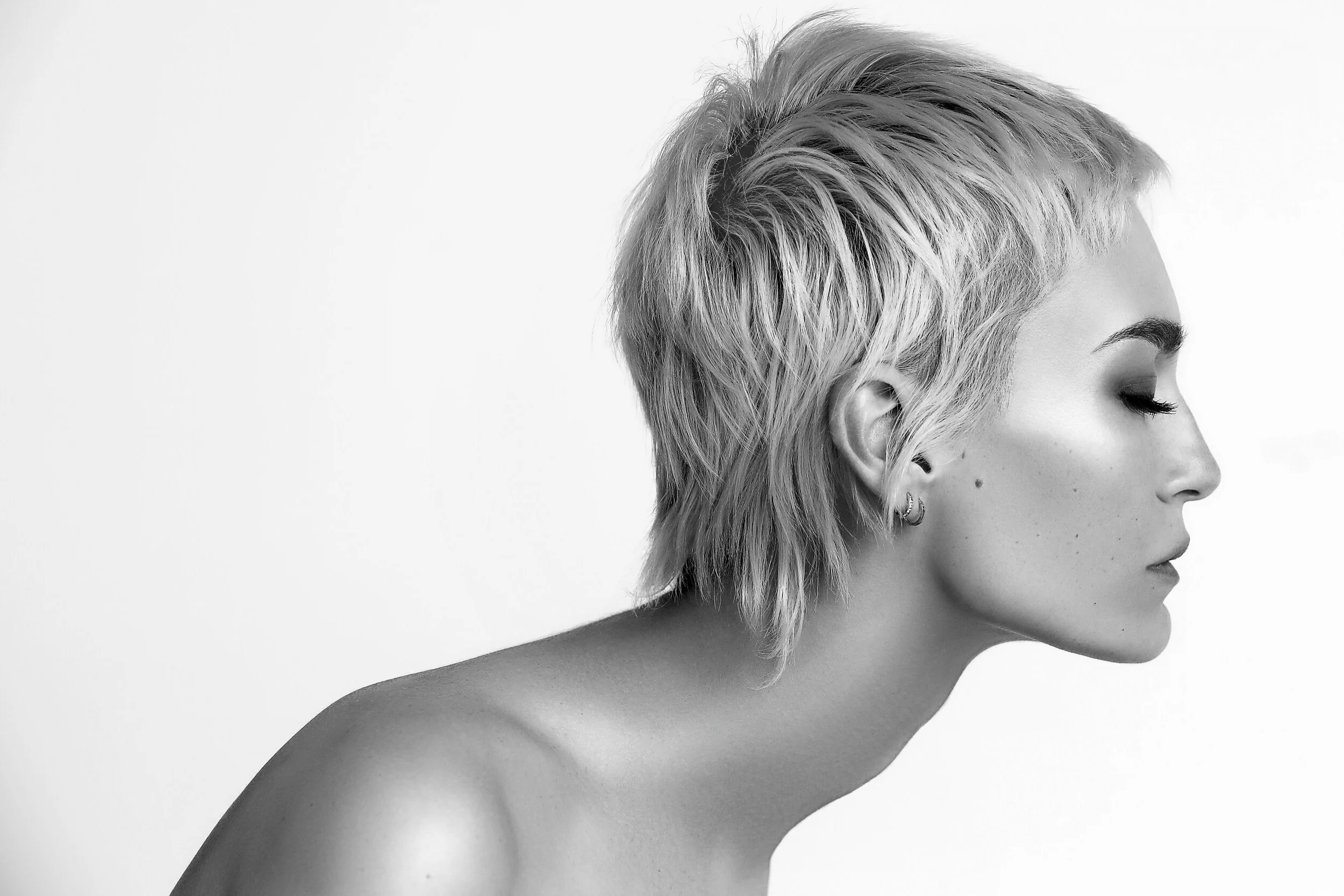 Black and white profile of a woman with short, tousled hair, closed eyes, and earrings, against a plain background. Model photographed by Los Angeles photographer Kenneth Dolin. Top Los Angele photographer specializing in model photography, beauty ph