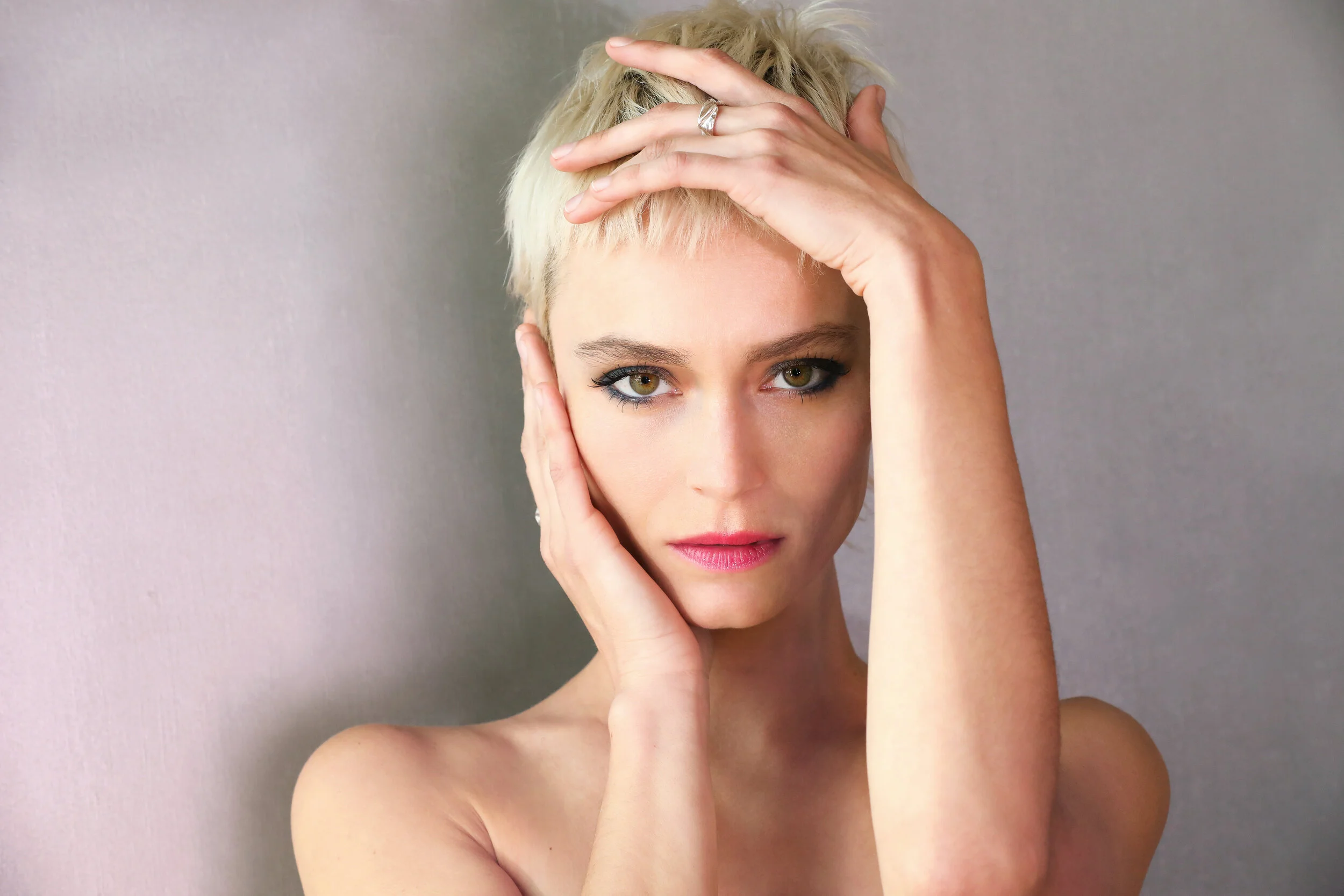 A woman with short blonde hair posing with her hands on her head and face, looking directly at the camera.Model photographed by Los Angeles photographer Kenneth Dolin. Top Los Angeles photographer specializing in model photography, beauty photography
