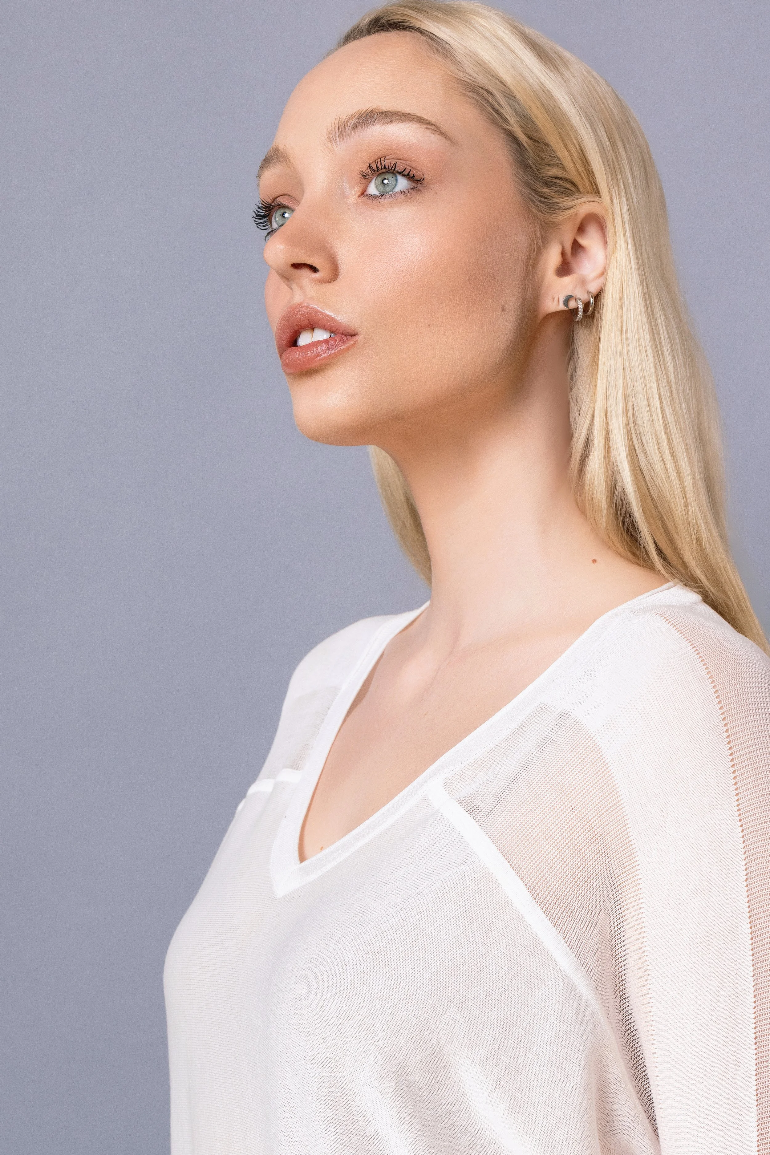 A portrait of a young woman with blonde hair and blue eyes, wearing a white top against a gray background.