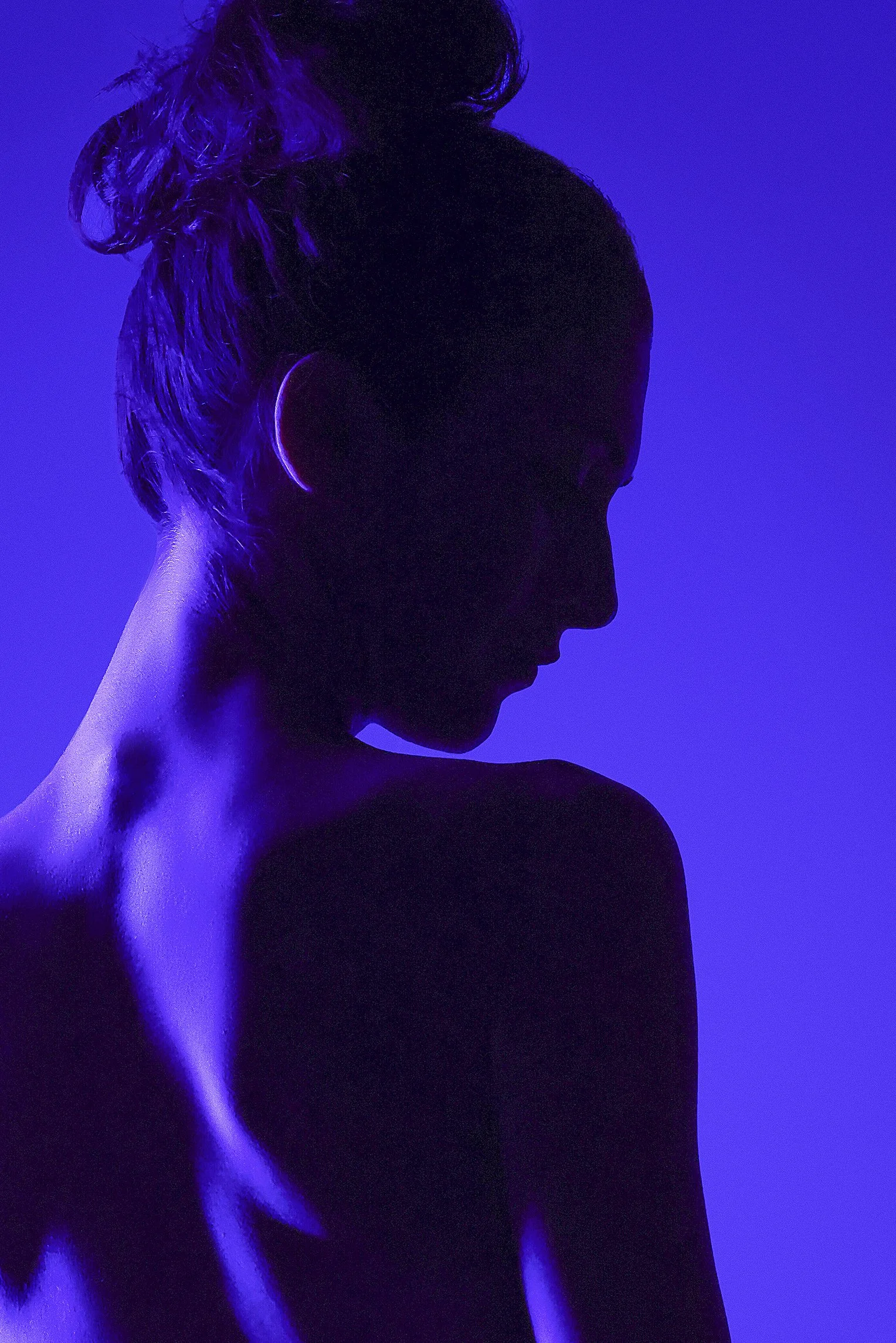 Silhouette of a woman with her hair in a bun, illuminated by purple-blue lighting, with her back and side profile visible. Photography by Kenneth Dolin, top Los Angeles headshot photographer. 