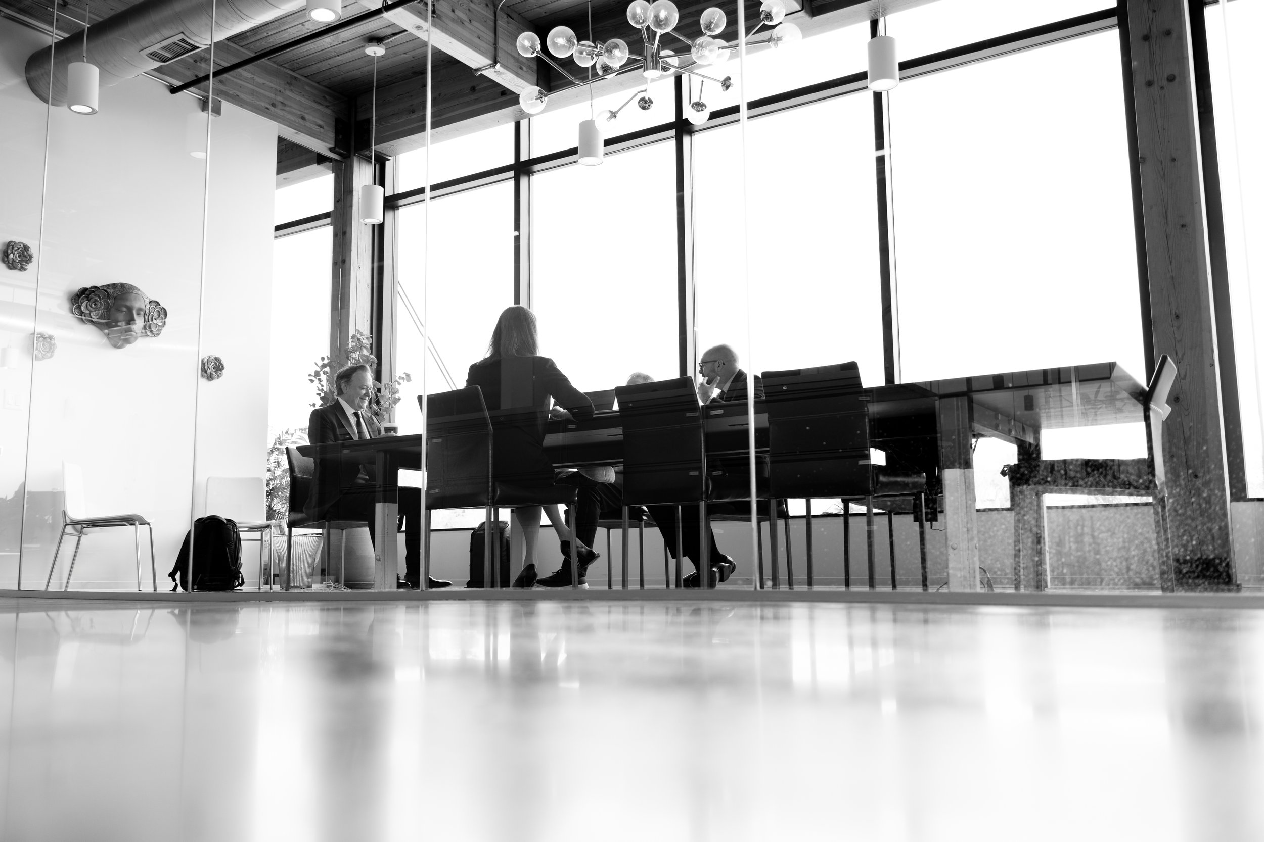 Business professionals engaged in a meeting in a modern office with floor to ceiling windows, pendant lighting, and decorative wall art.
