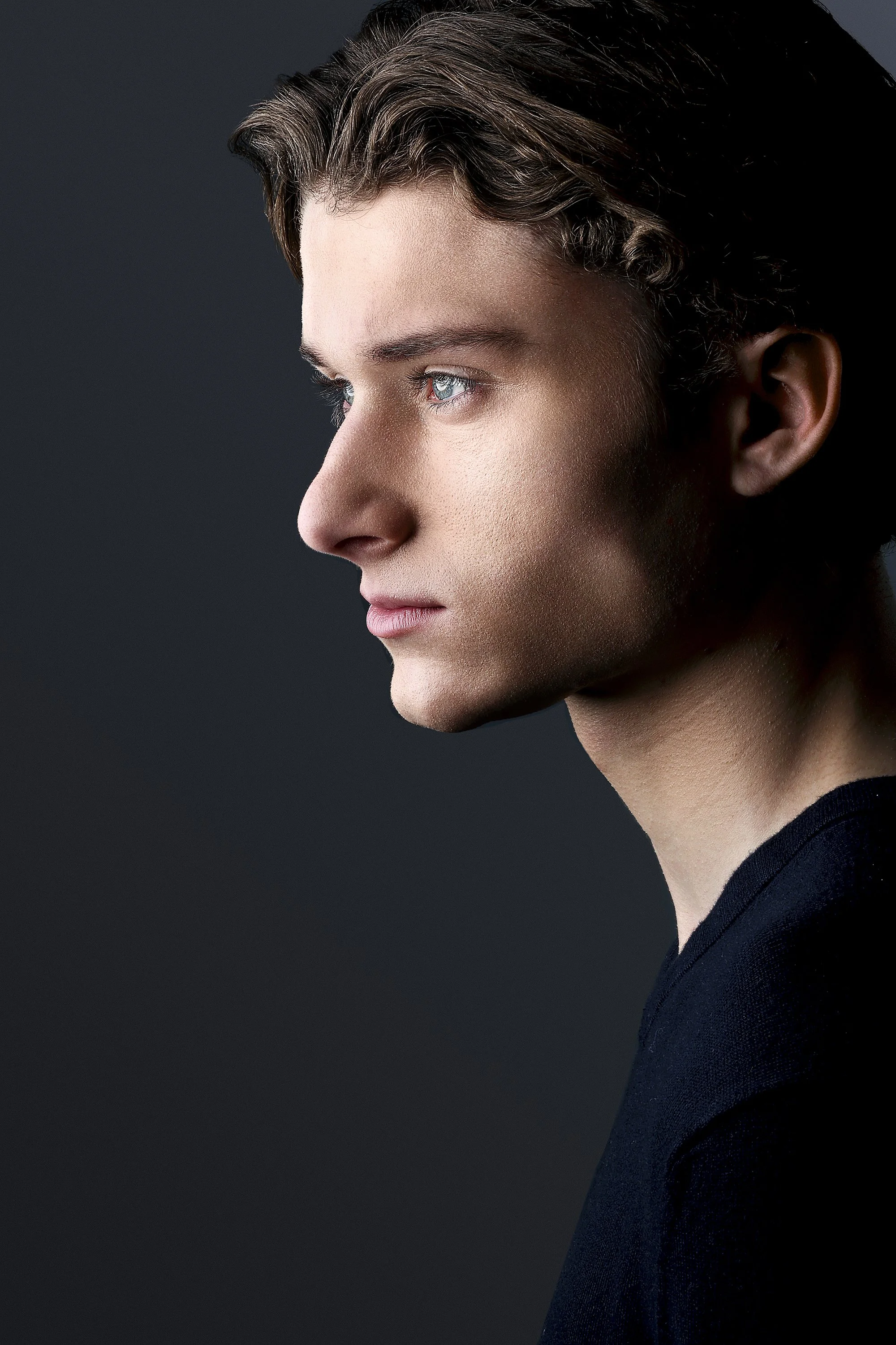 Side profile of a young man with light skin, brown hair, and blue eyes against a dark background.  Image by top Los Angeles photographer Kenneth Dolin. 