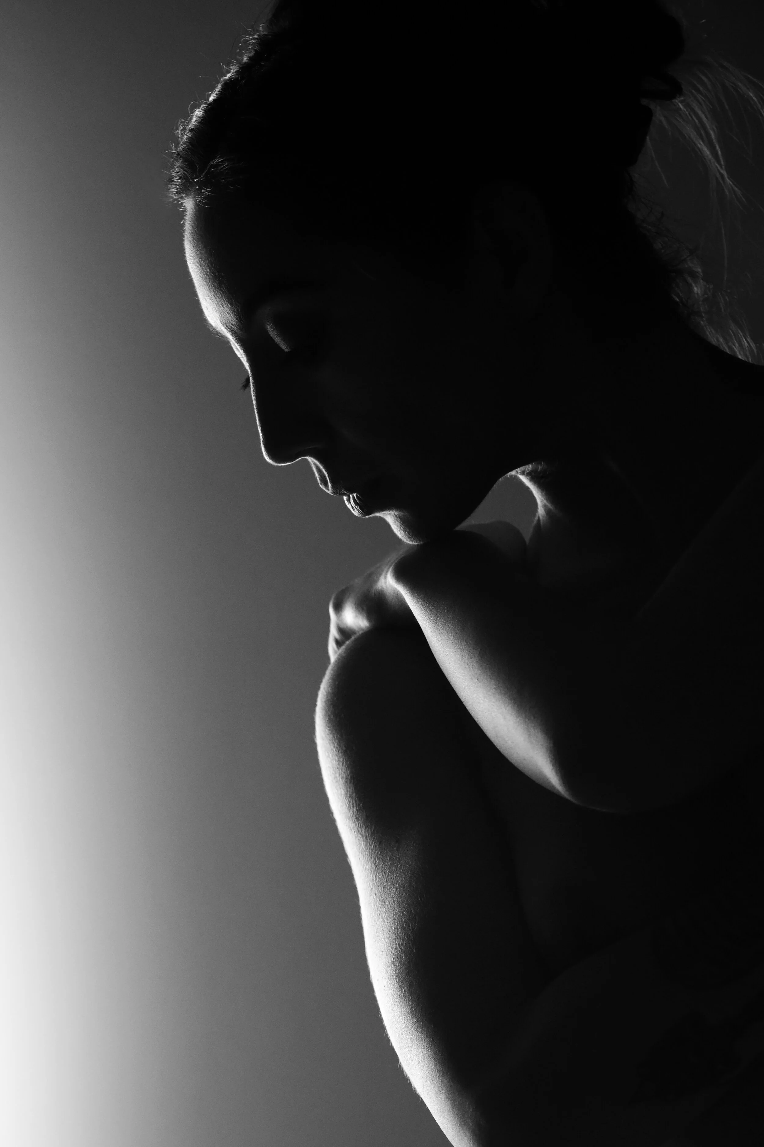 Black and white silhouette of a woman with her eyes closed, touching her shoulder, with light source behind her creating contrast.
