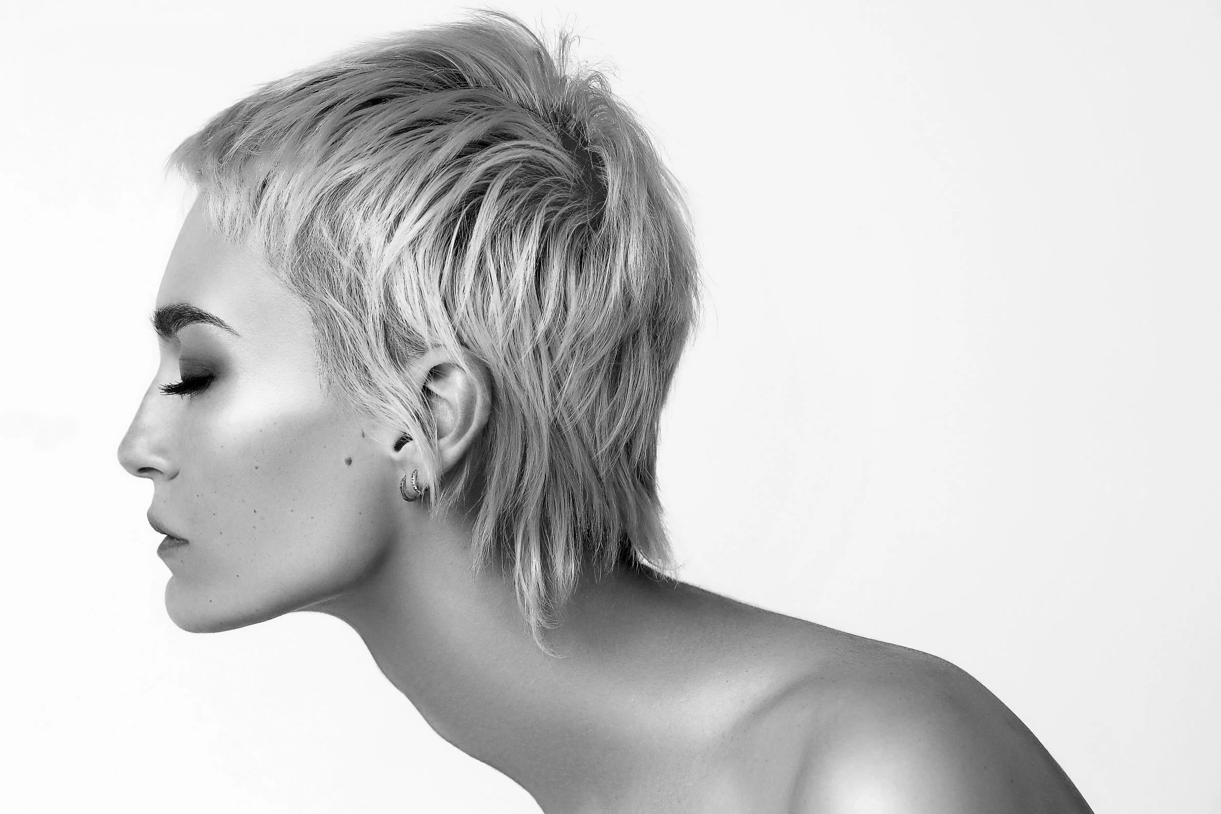 Black and white side profile of a woman with short, styled hair and earrings, against a plain background.