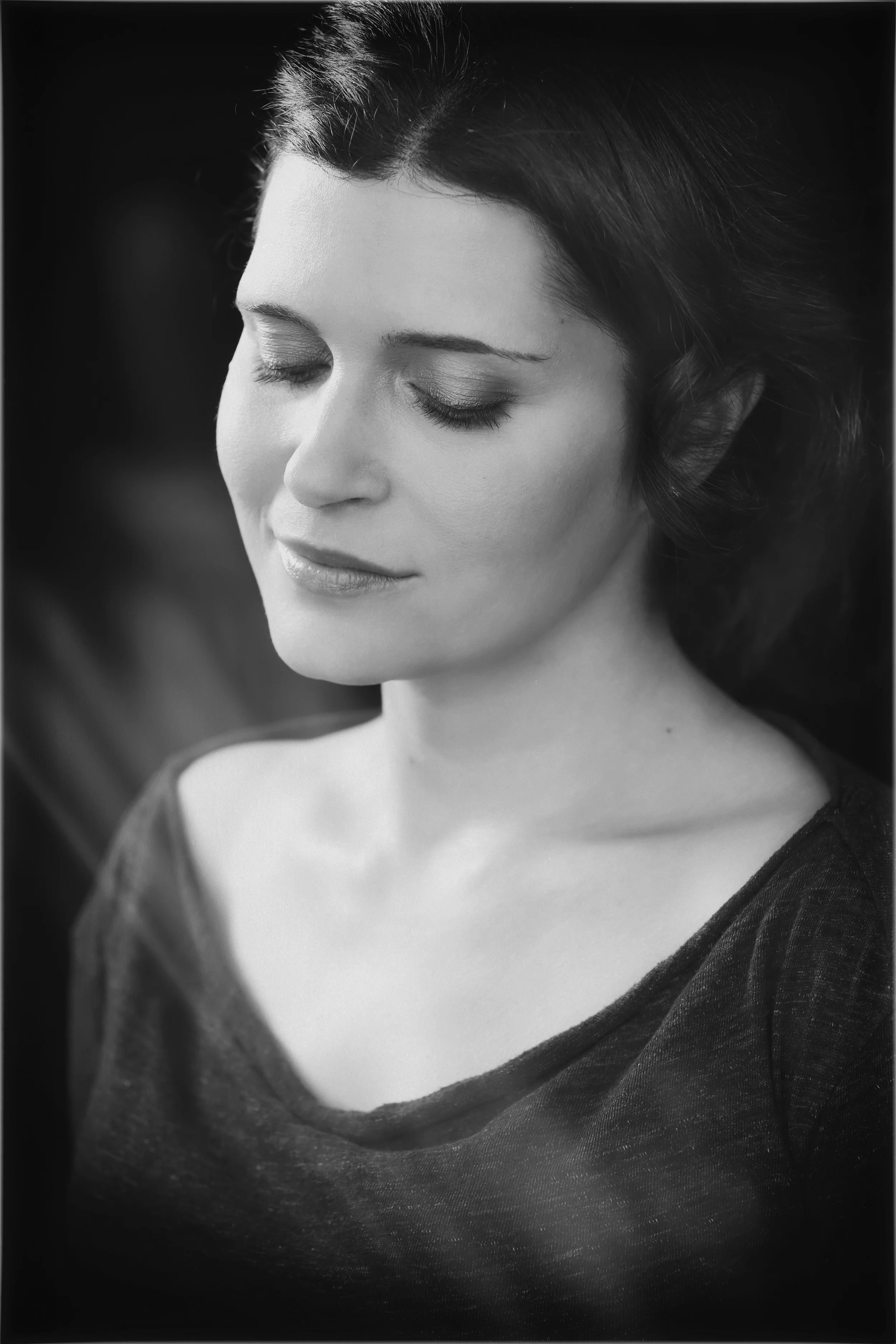 Black and white portrait of a woman with eyes closed, smiling softly, wearing a dark top.  Image by top Los Angeles photographer Kenneth Dolin. 